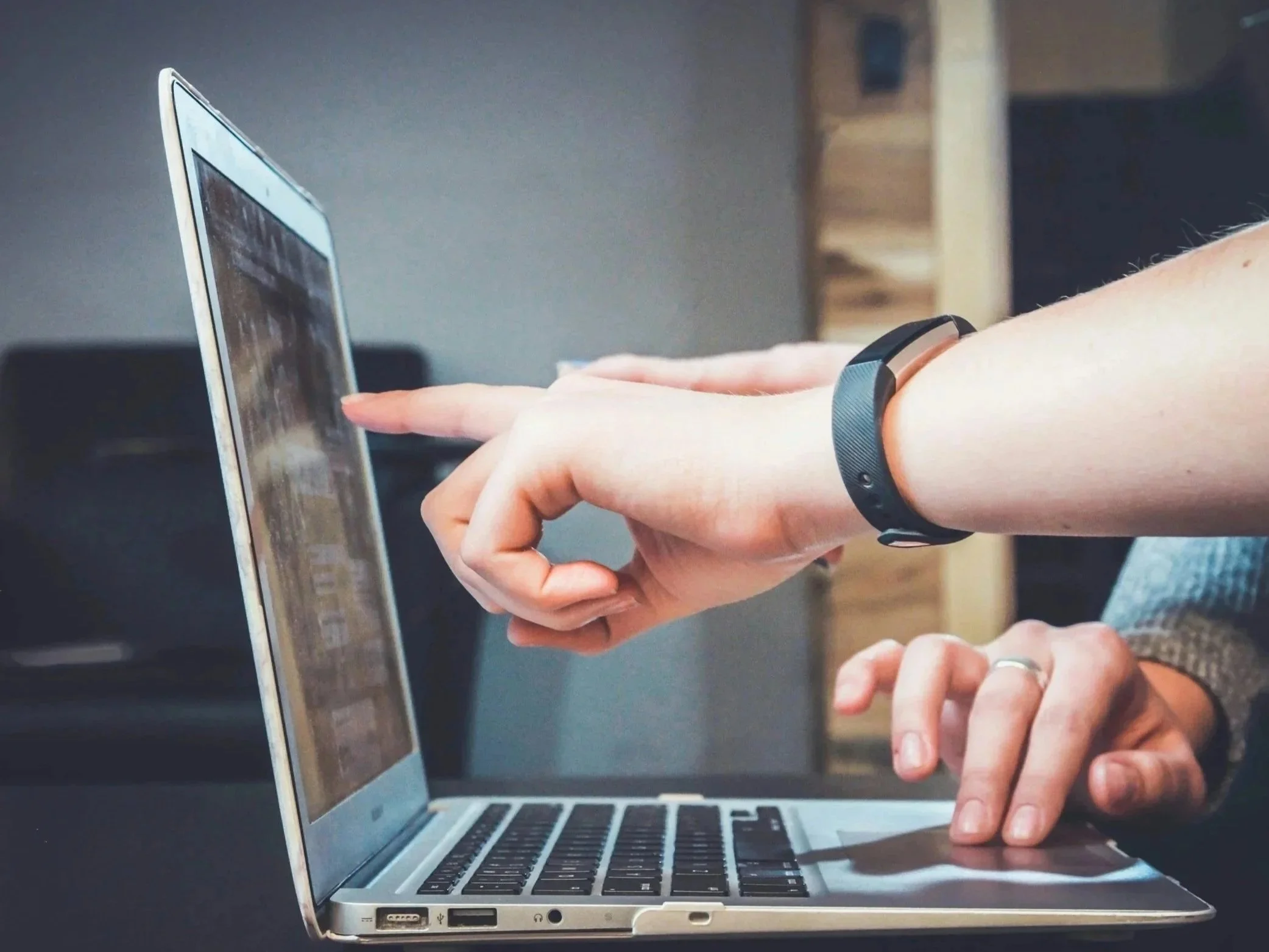 People consulting using a laptop and pointing at the screen, wearing a fitness tracker on their wrist.