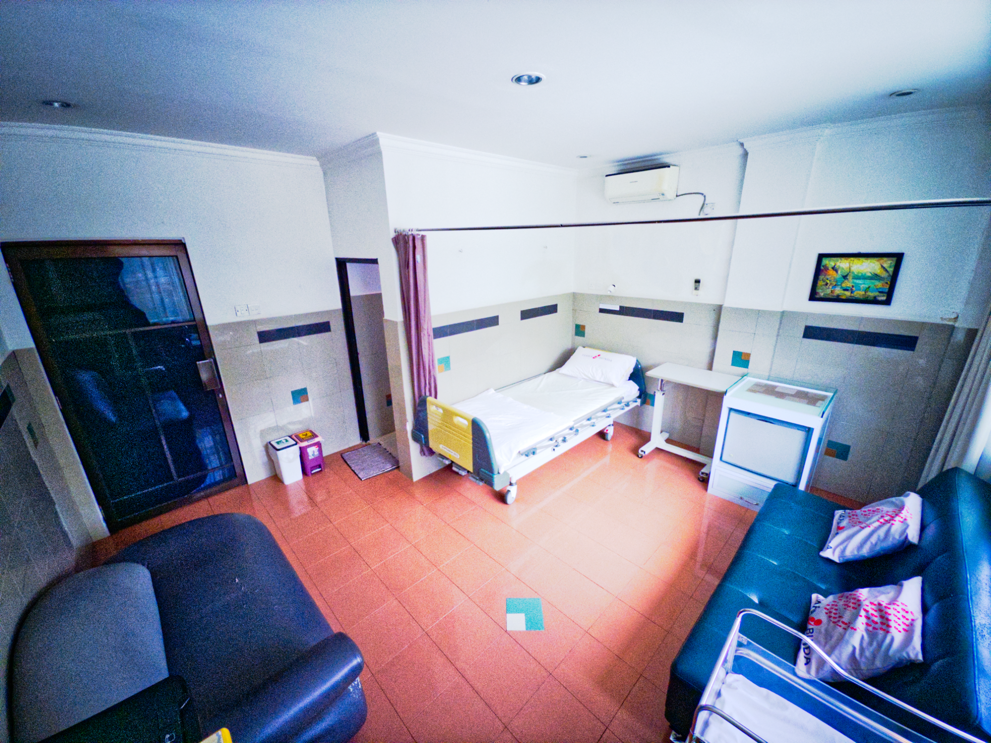 Hospital room with a hospital bed, a couch, and medical equipment.