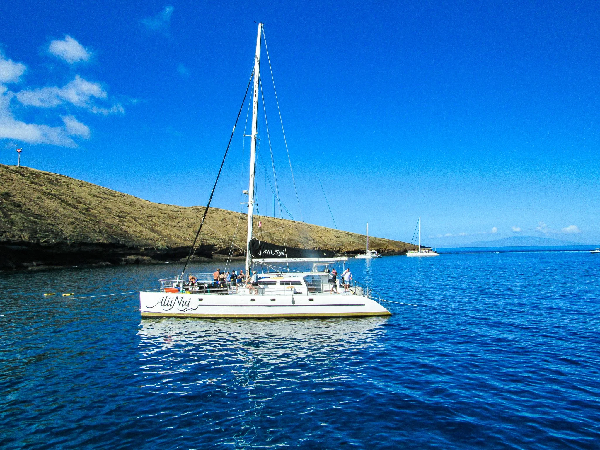 Alii Nui luxury sailing catamaran anchored inside Molokini Crater off the South Maui coast with the volcanic crater and Pacific Ocean in view.