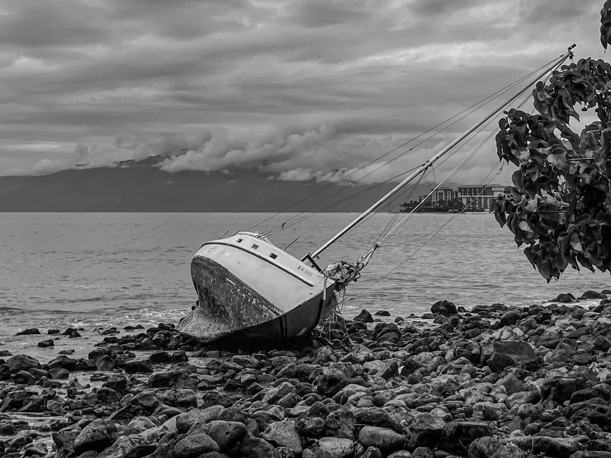 Black and white boat wreck along the Lahaina Maui coastline resting on rocky shore with ocean and cloudy sky in the background
