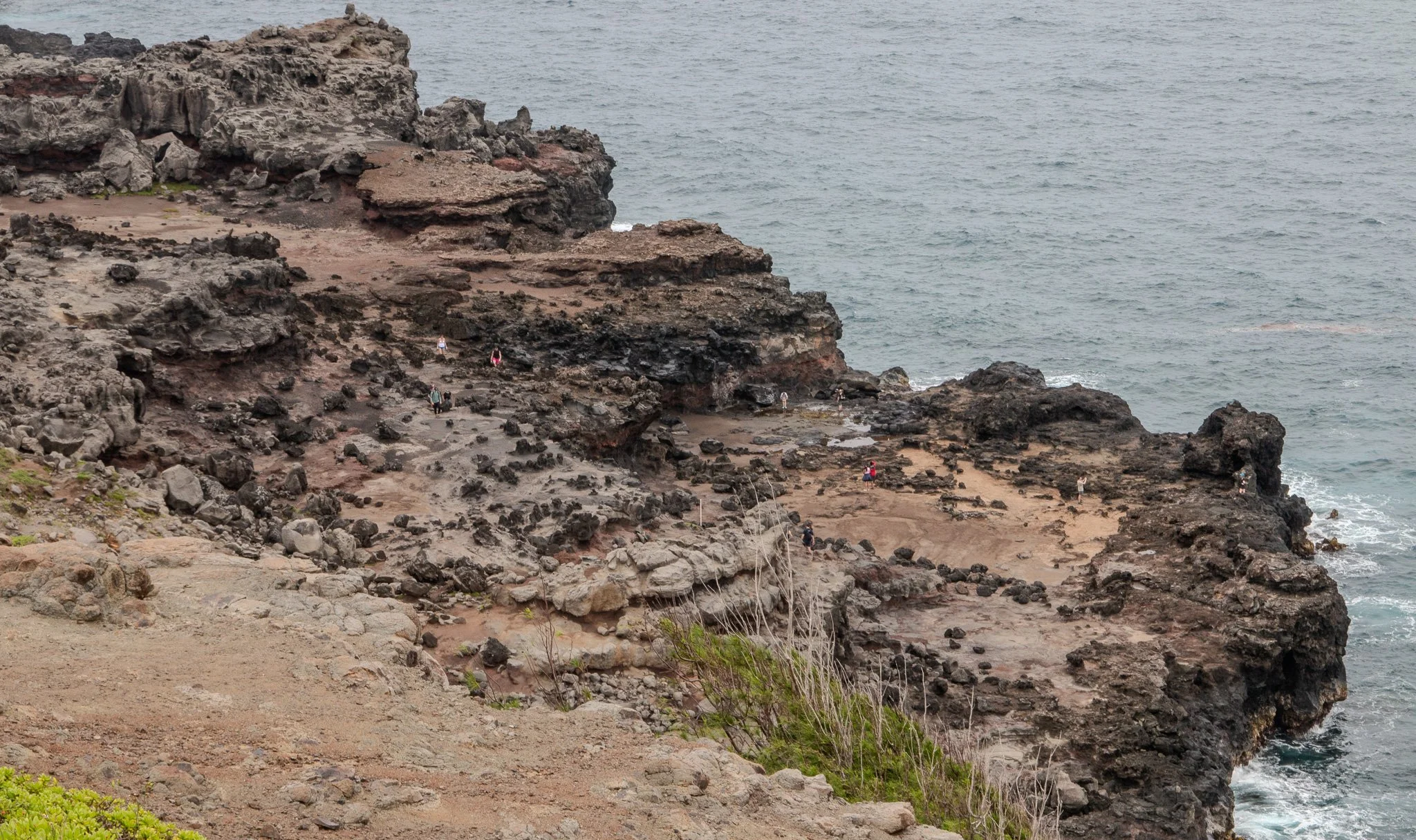 Visitors exploring the rugged lava rock coastline surrounding Nakalele Blowhole on Maui’s northwest shore in the West Maui Mountains.