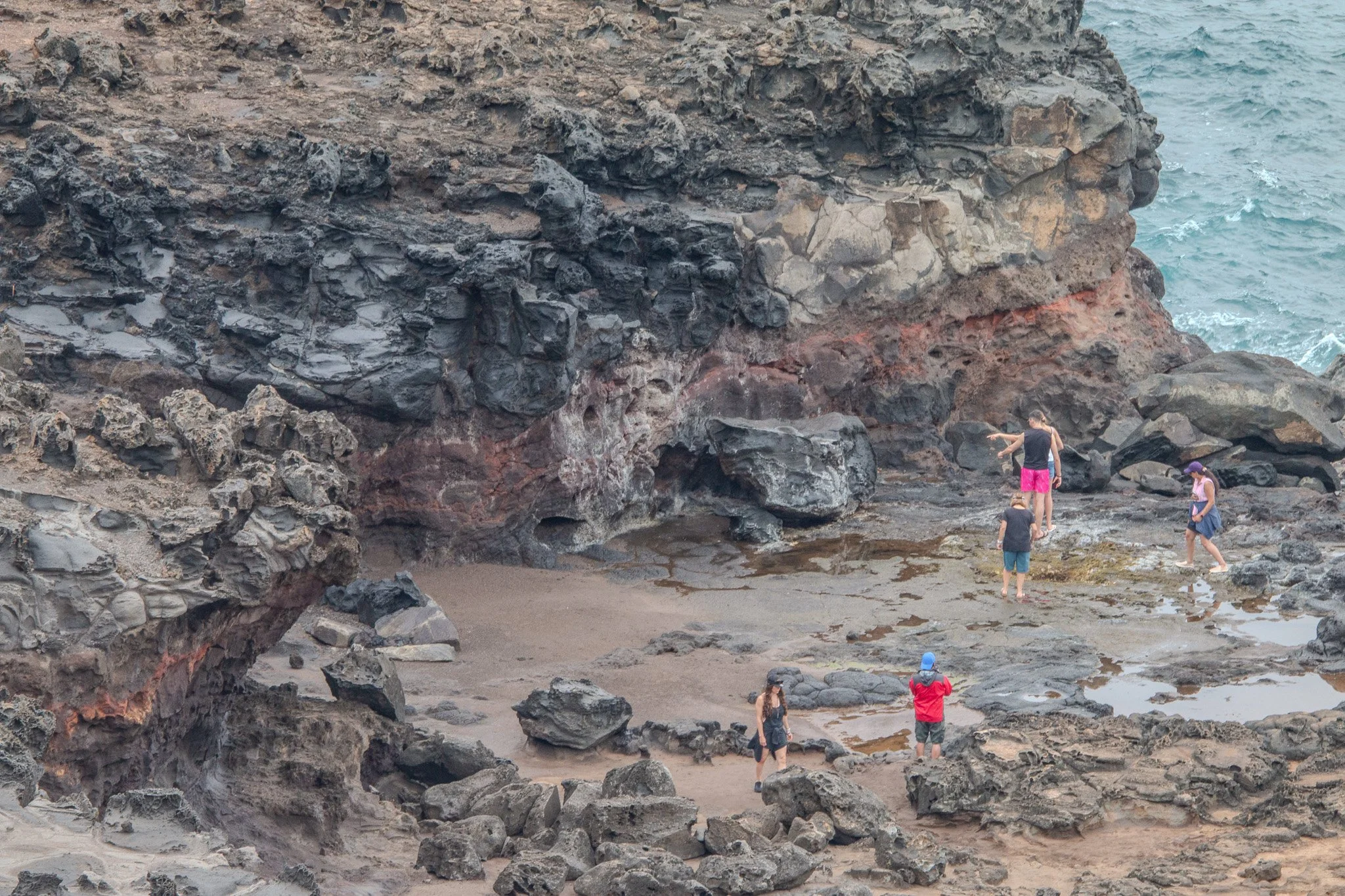 Visitors exploring eroded volcanic lava cliffs and tidal pools near Nakalele Blowhole on Maui’s rugged northwest coastline.