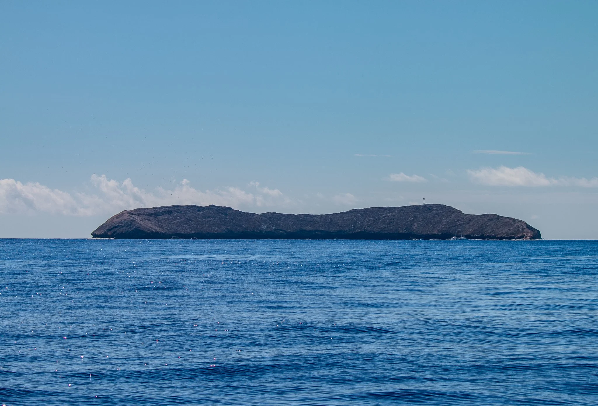 Molokini Crater seen from Maui’s southern coastline, its partially submerged crescent shape visible above the Pacific horizon.