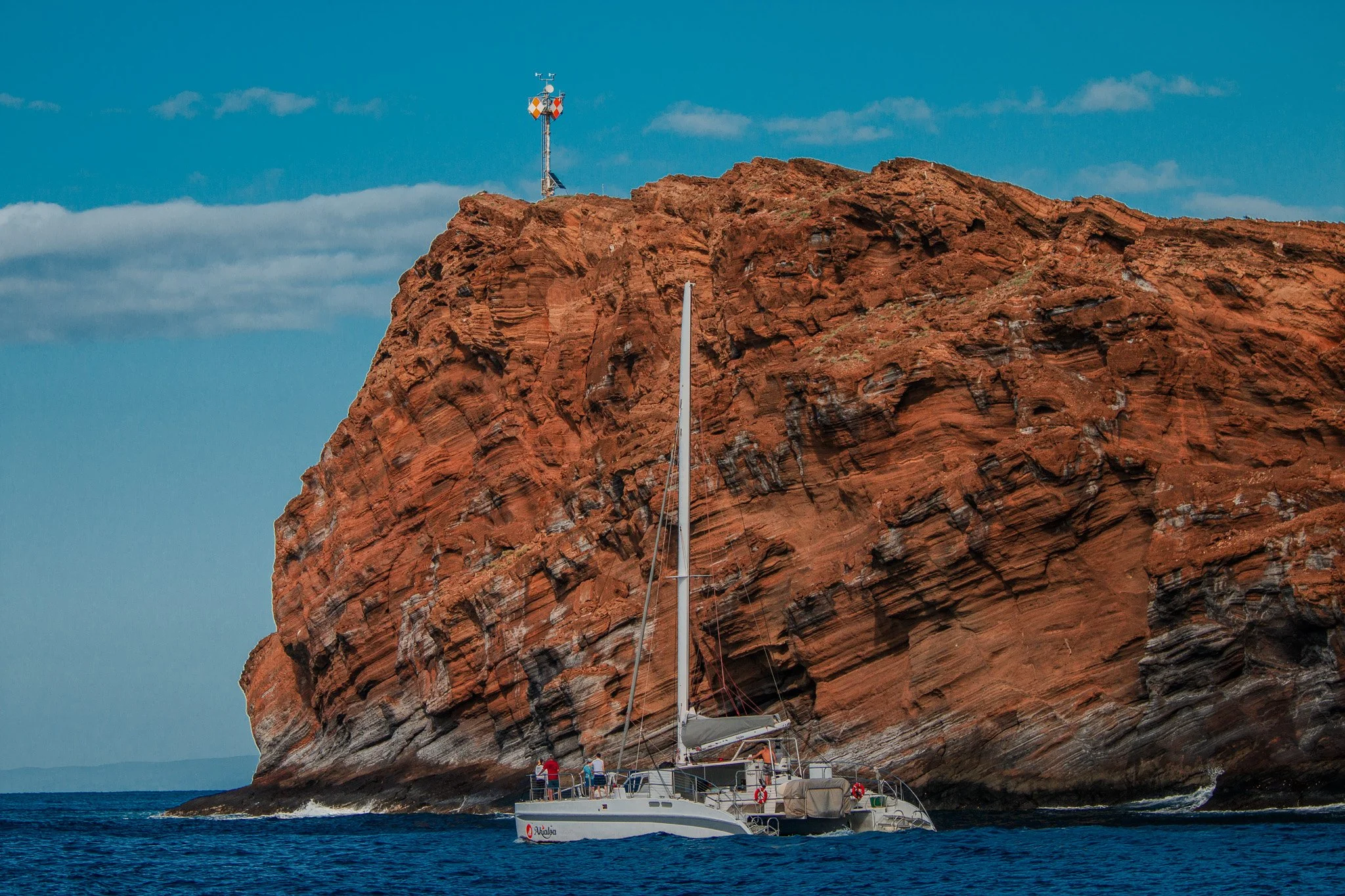 
Catamaran sailboat maneuvering beside the towering red rear volcanic cliffs of Molokini Crater, one of Maui’s most recognizable offshore landmarks.