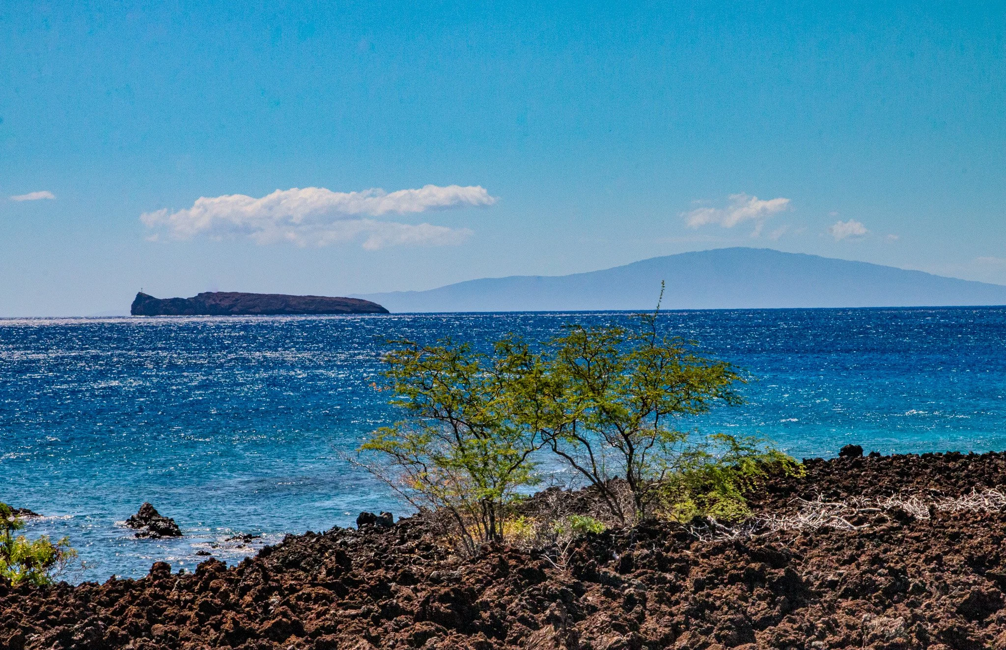 Molokini Crater viewed from La Perouse Bay lava coastline with Kahoʻolawe island in the distance off the south coast of Maui, Hawaii.