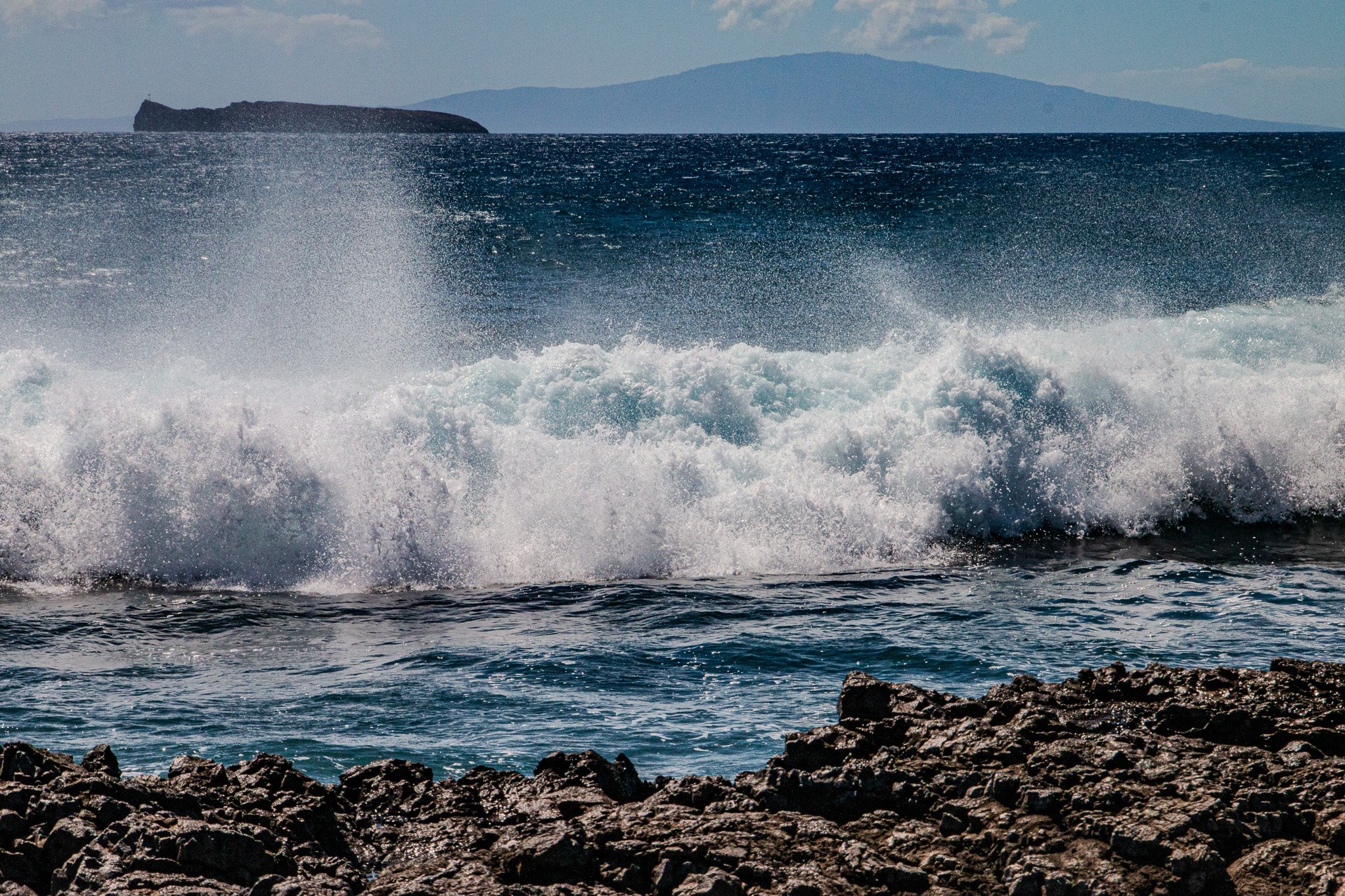 Waves breaking along Maui’s La Perouse Bay lava shoreline with Molokini Crater visible offshore across the open Pacific.