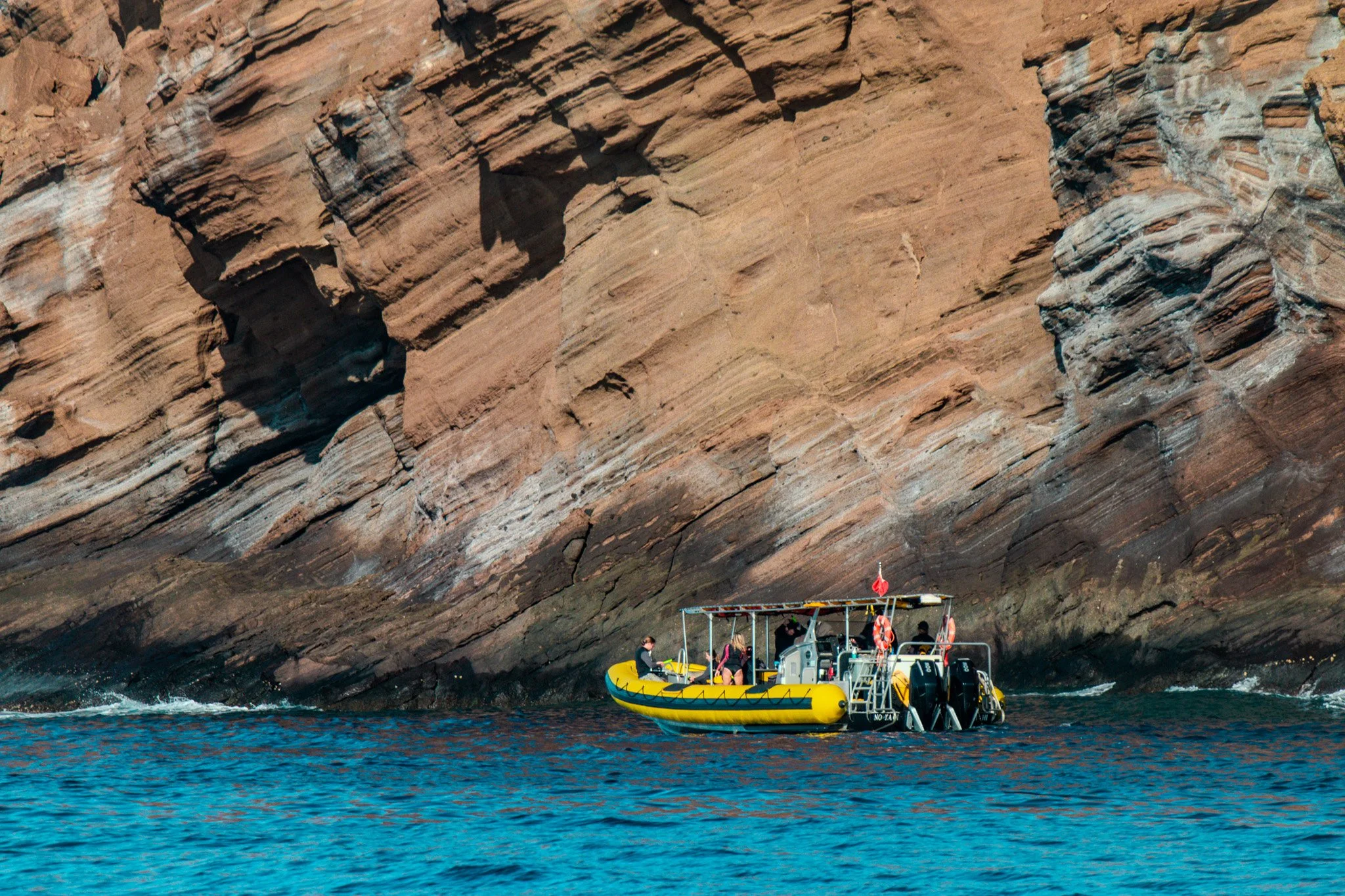Diving raft exploring the rugged often not seen back side cliffs of Molokini Crater, where volcanic rock walls drop sharply into clear Pacific waters.