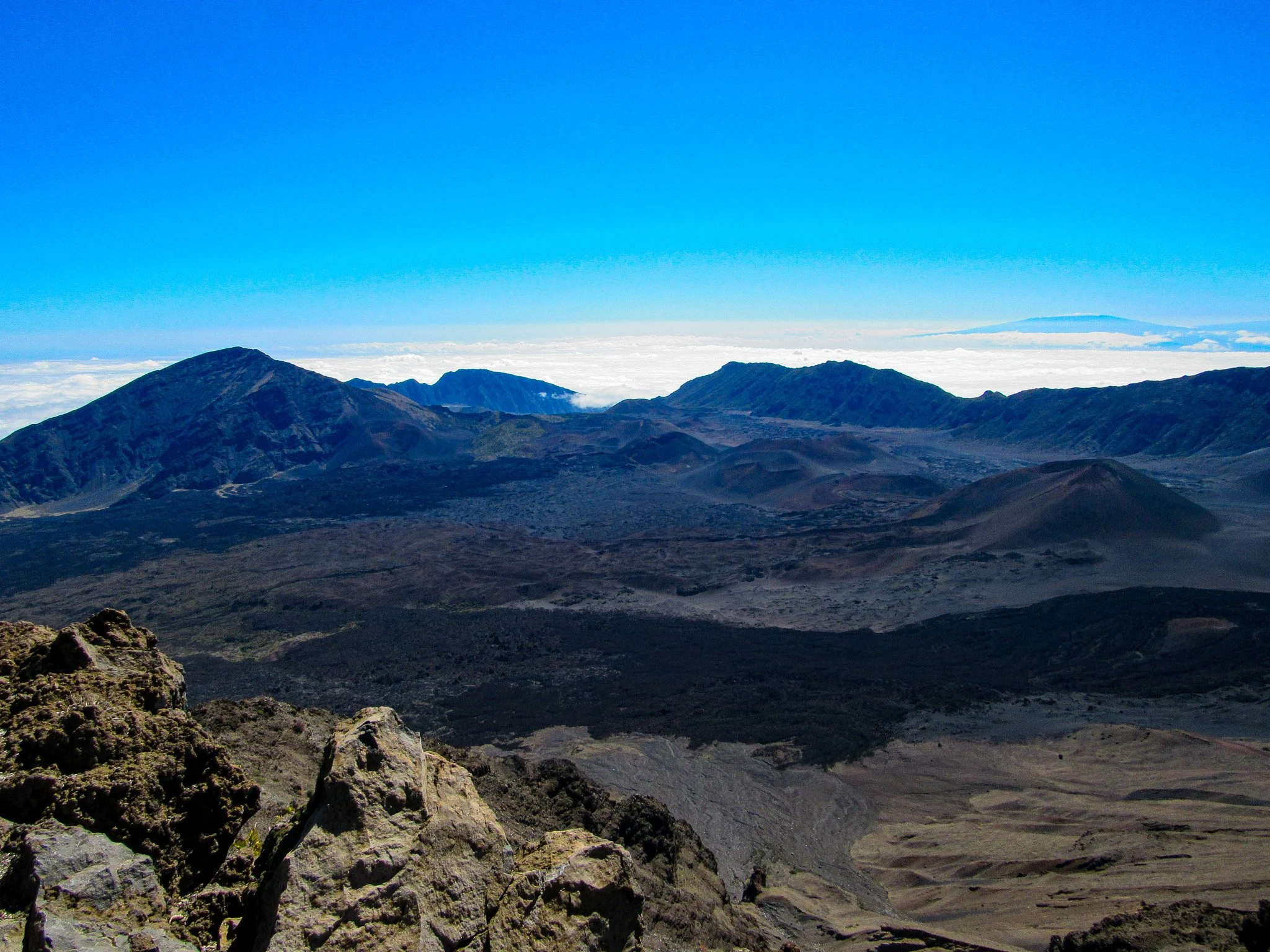A mountain landscape with volcanic peaks and a clear blue sky, with some clouds near the horizon.