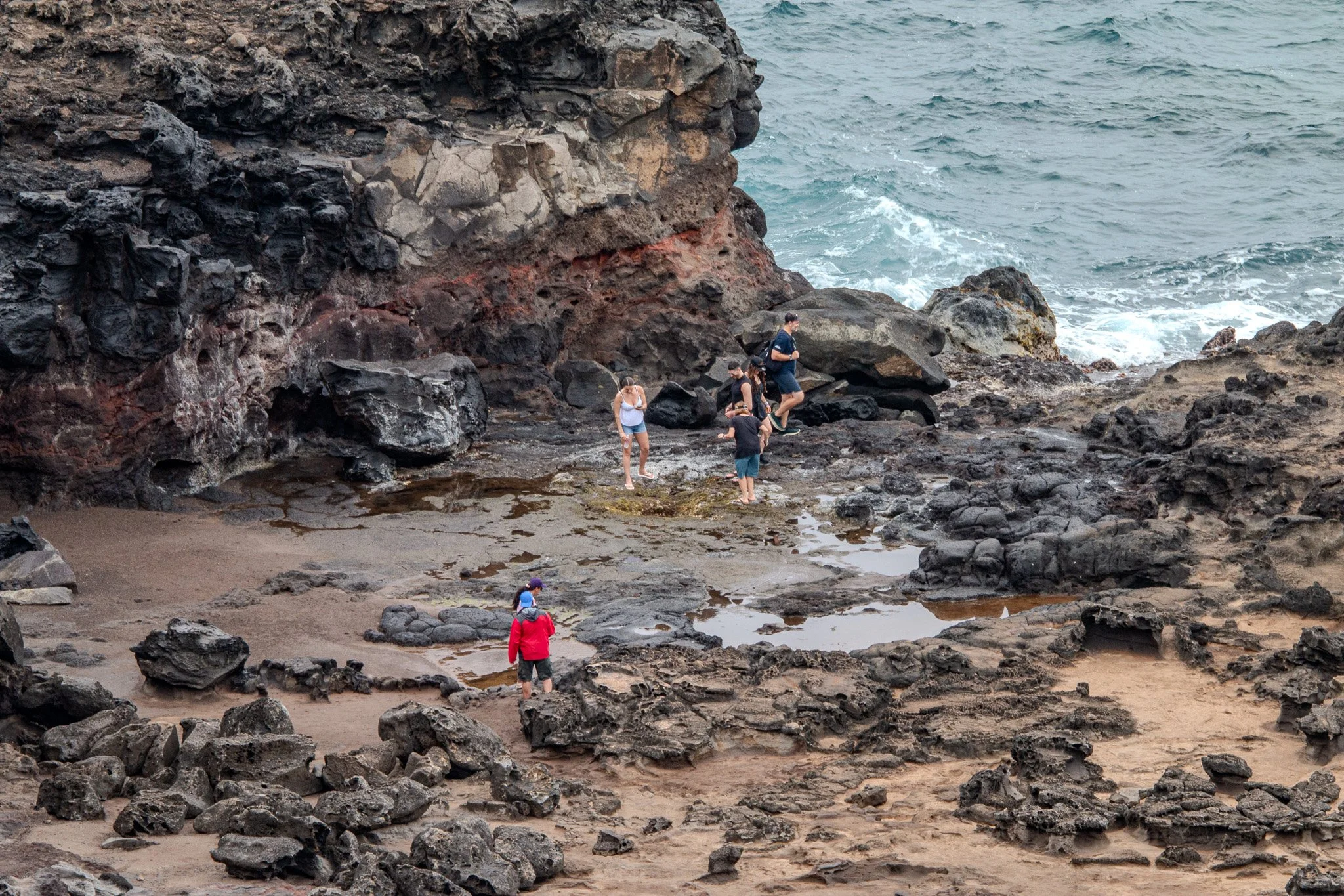 Visitors standing on rugged lava rock near Nakalele Blowhole on Maui’s northwest coast, a powerful ocean blowhole formed by volcanic shoreline erosion.