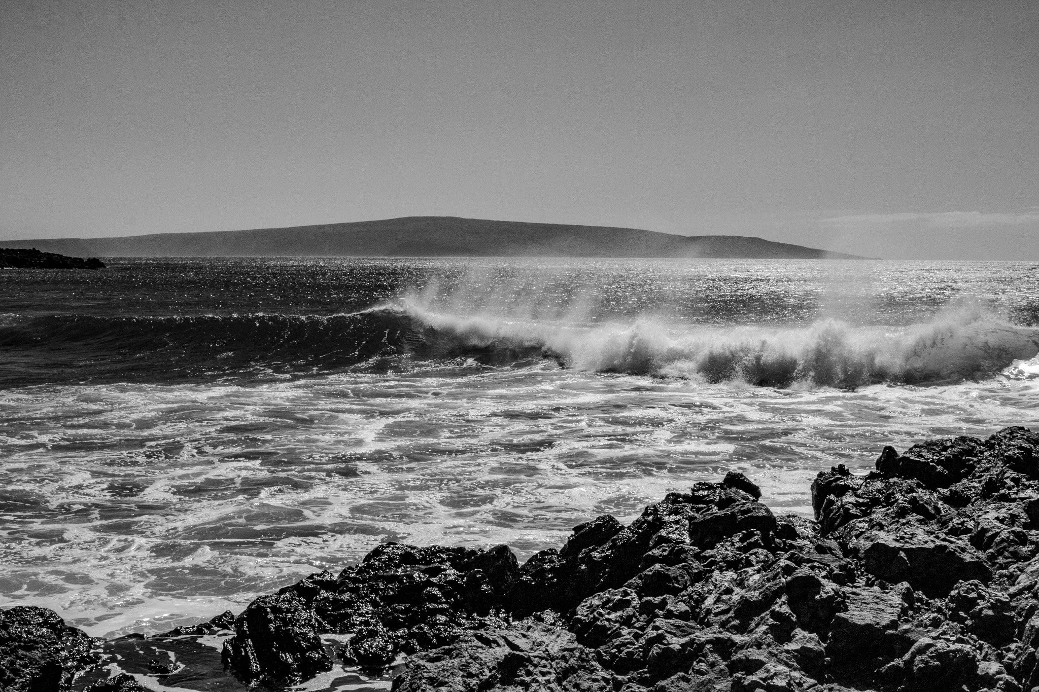 Black and white breaking wave at La Perouse Bay in Maui with sunlight reflecting off the ocean and lava rock shoreline in the foreground