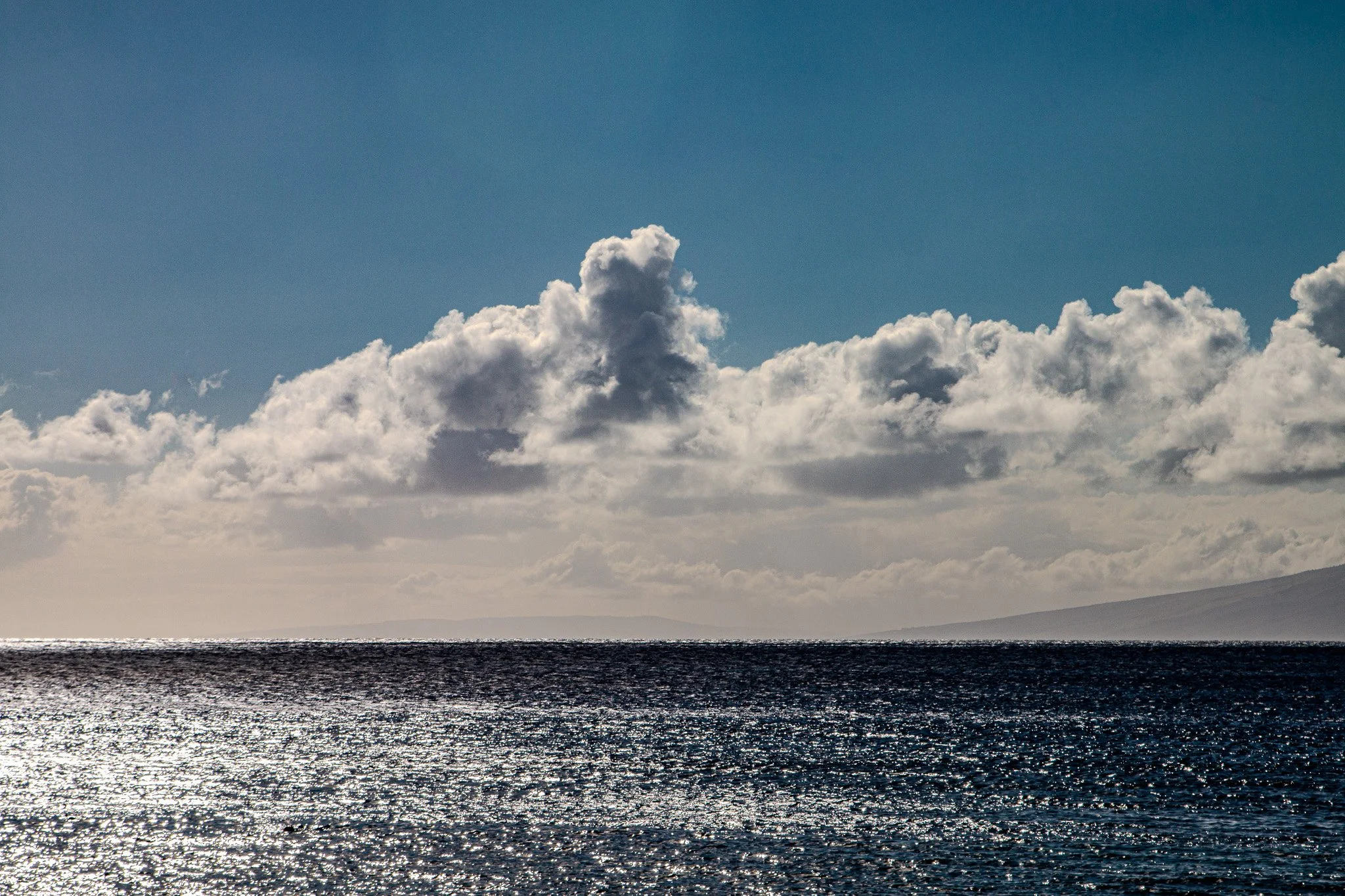 Towering trade-wind clouds above Molokaʻi on the Pacific horizon viewed from Kāʻanapali Beach, West Maui.