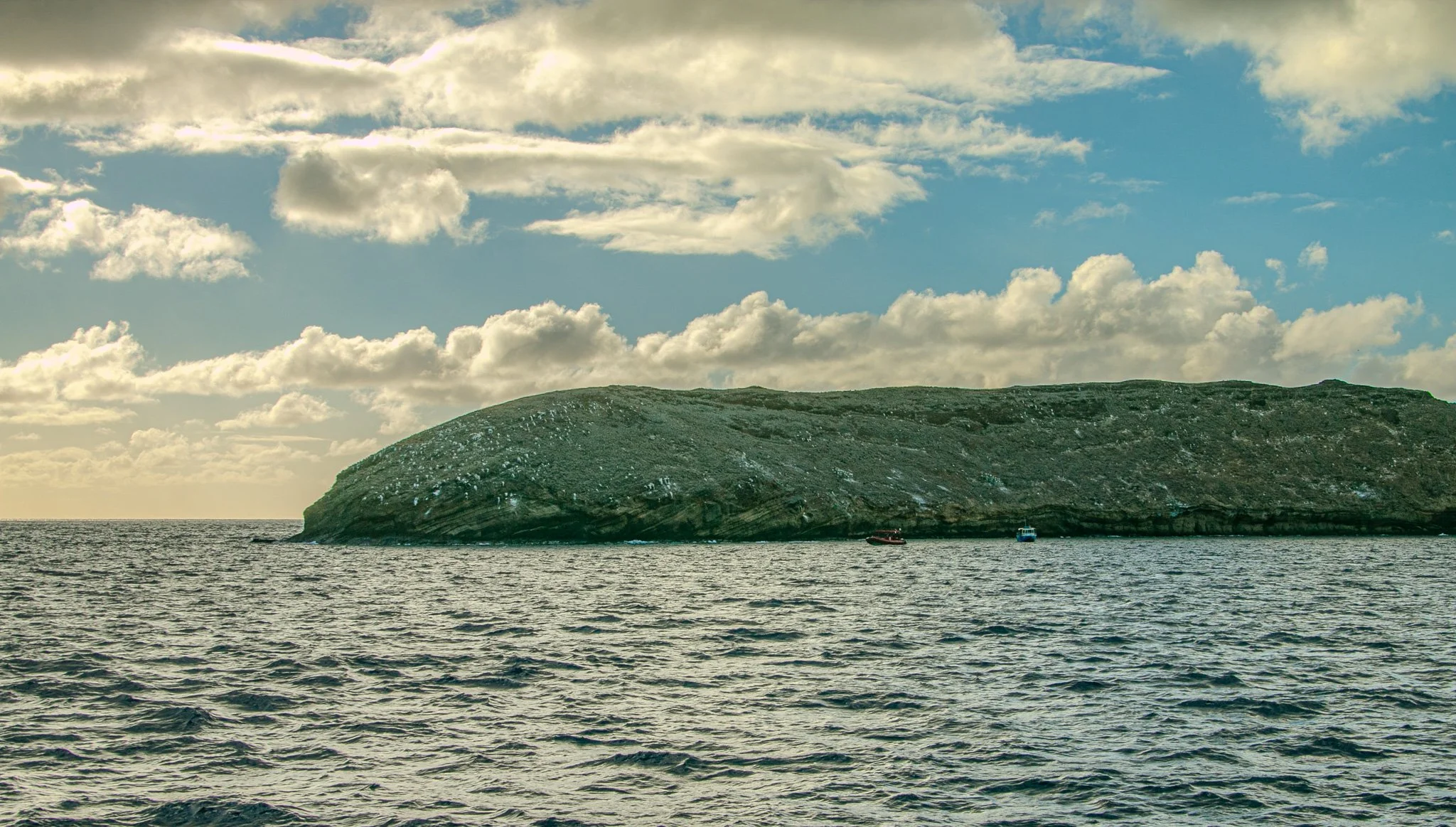Clouds drifting above Molokini Crater, viewed across the deep blue waters between Maui and the offshore volcanic crescent.

