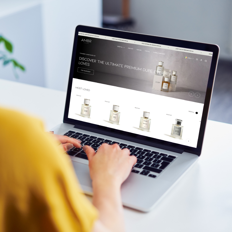 Person in yellow shirt browsing perfume products on a laptop with an online store.