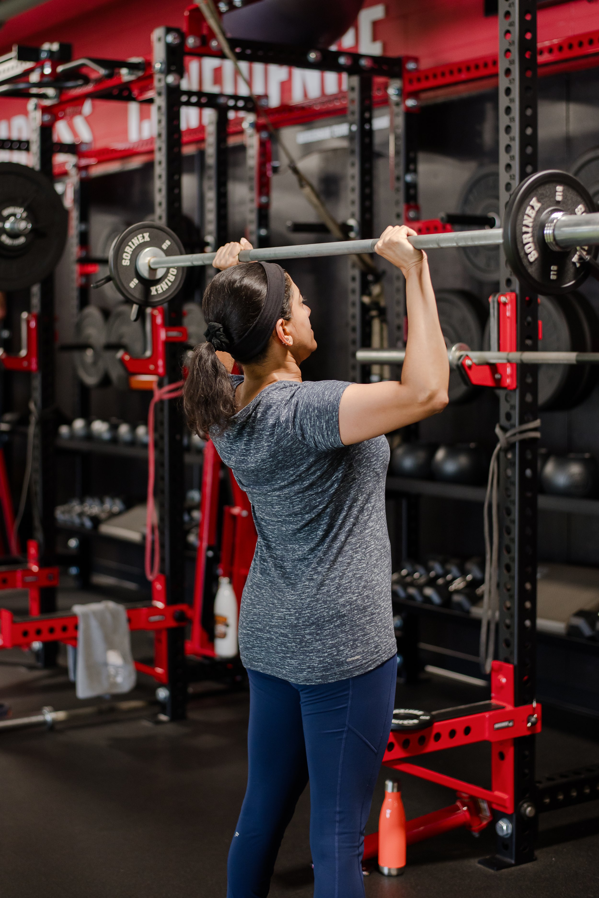 A woman lifting a barbell in a gym.