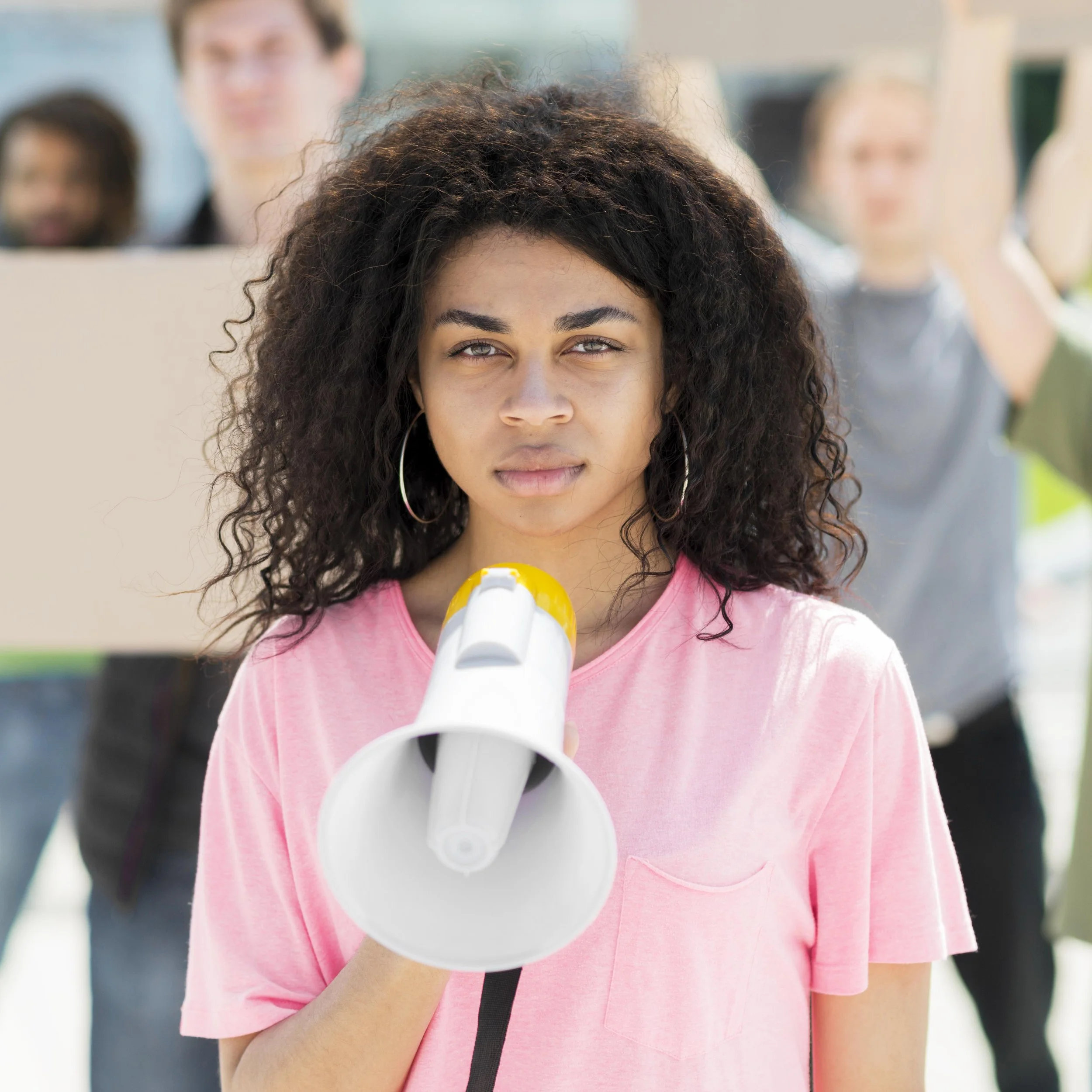 Young woman holding a megaphone at a protest or rally, with other people holding signs in the background.