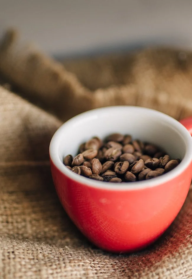 Red coffee cup filled with coffee beans on a burlap surface.