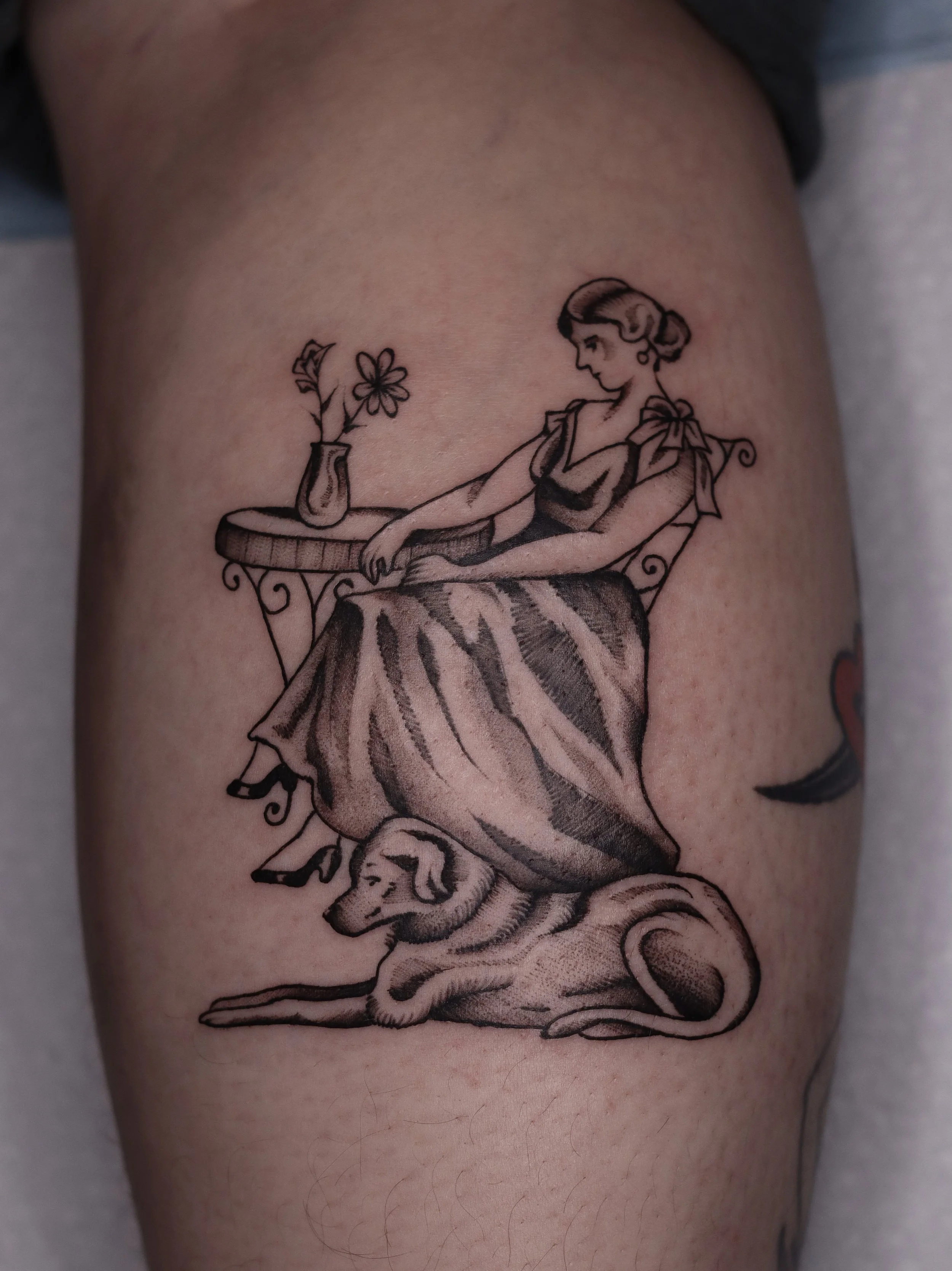 Tattoo of a woman in a dress, a table with a vase of flowers, and a dog laying down 