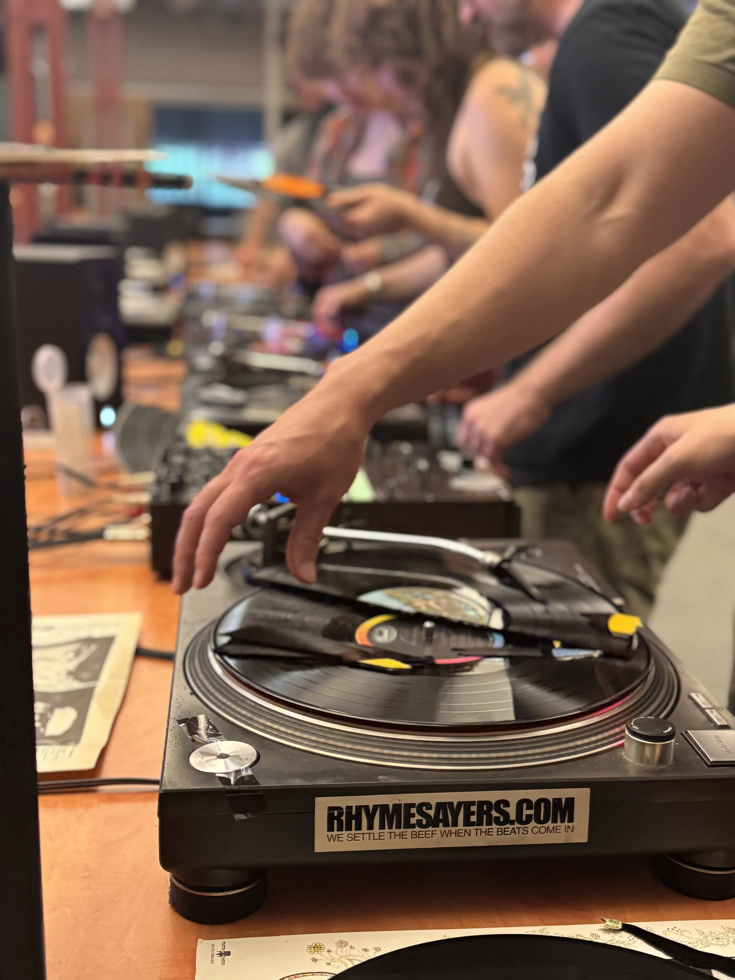 Close-up of a DJ's turntable and mixer with a person operating the equipment at a free turntable workshop for musicians