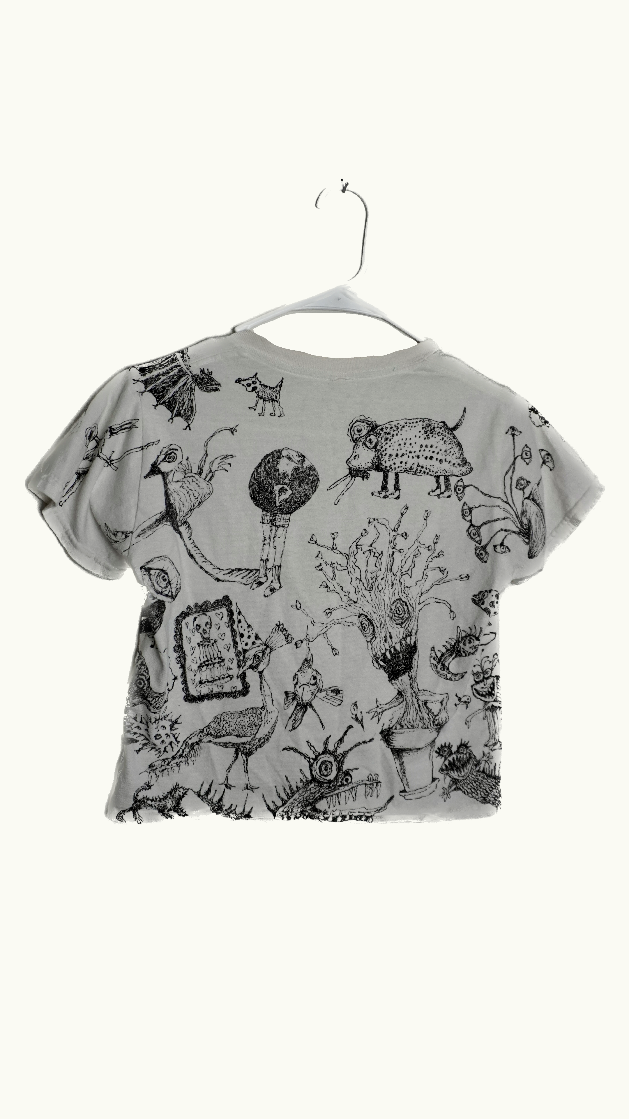 A white t-shirt with black illustrations of various fantastical creatures and characters, hanging on a white hanger against a plain background.