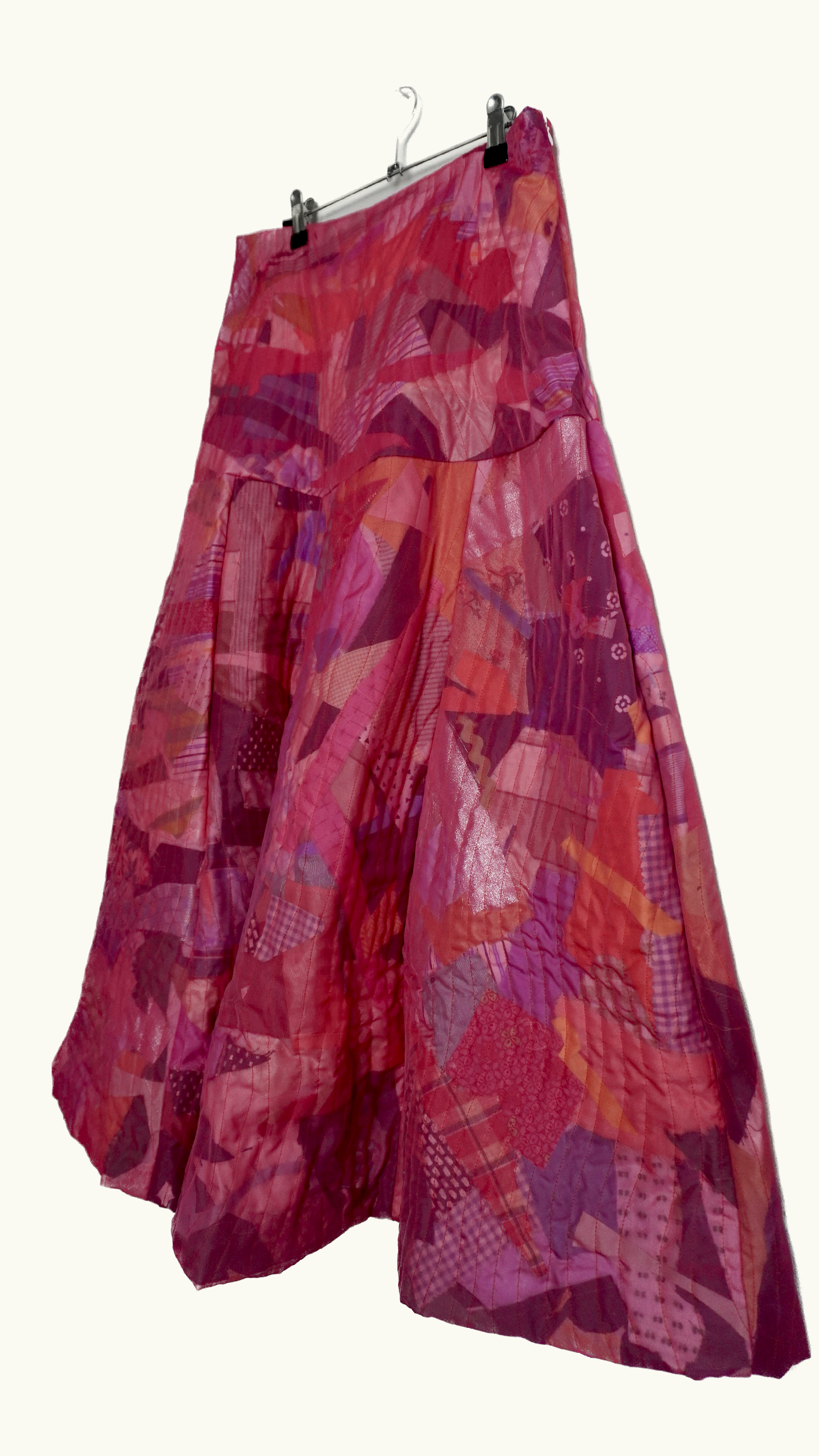 A long, flowing skirt with a colorful patchwork pattern in shades of pink, red, and purple hanging on a hanger.