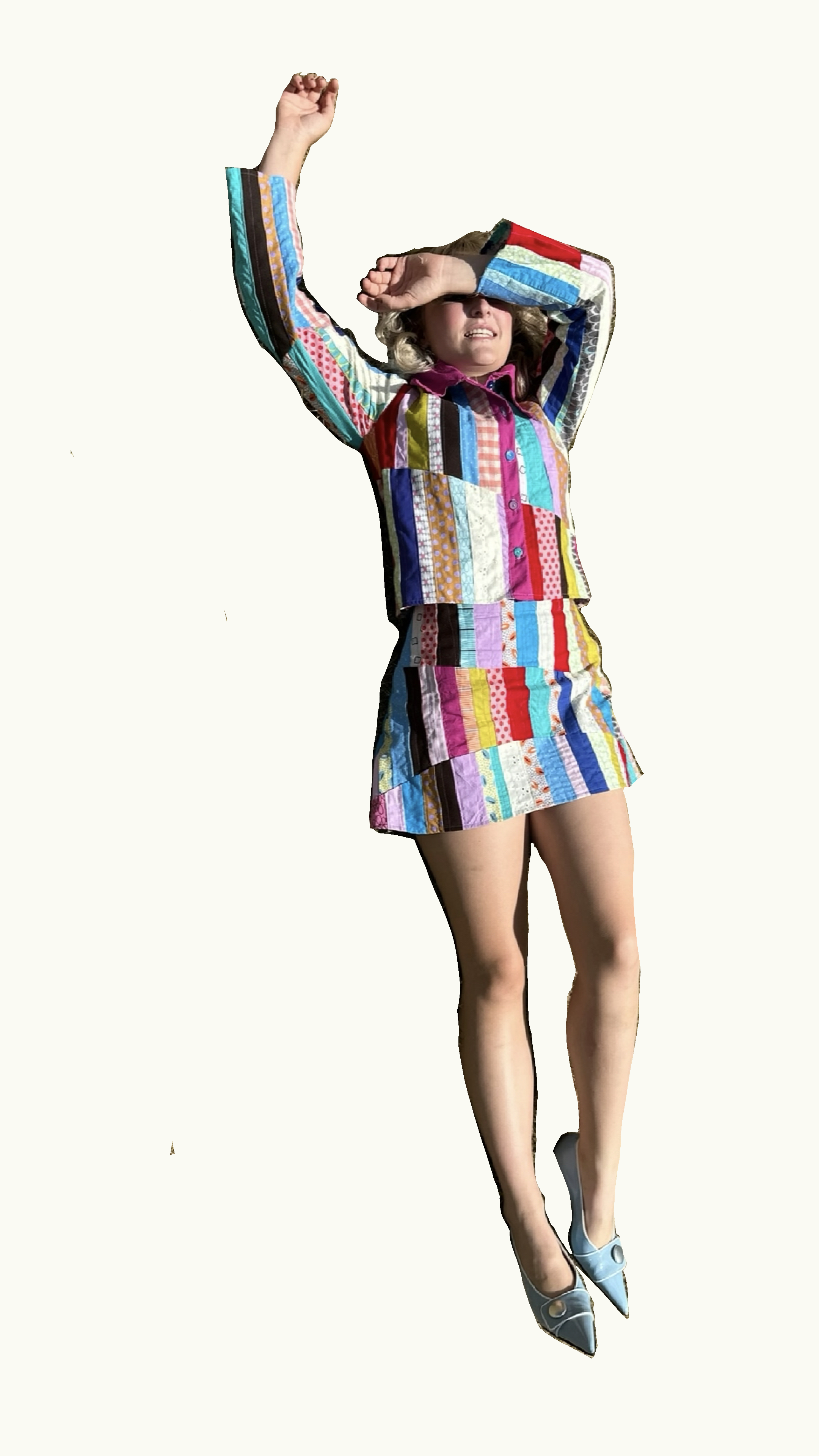 A woman is wearing a colorful, patchwork matching top and skirt with high heels and is shielding her eyes with her arm.