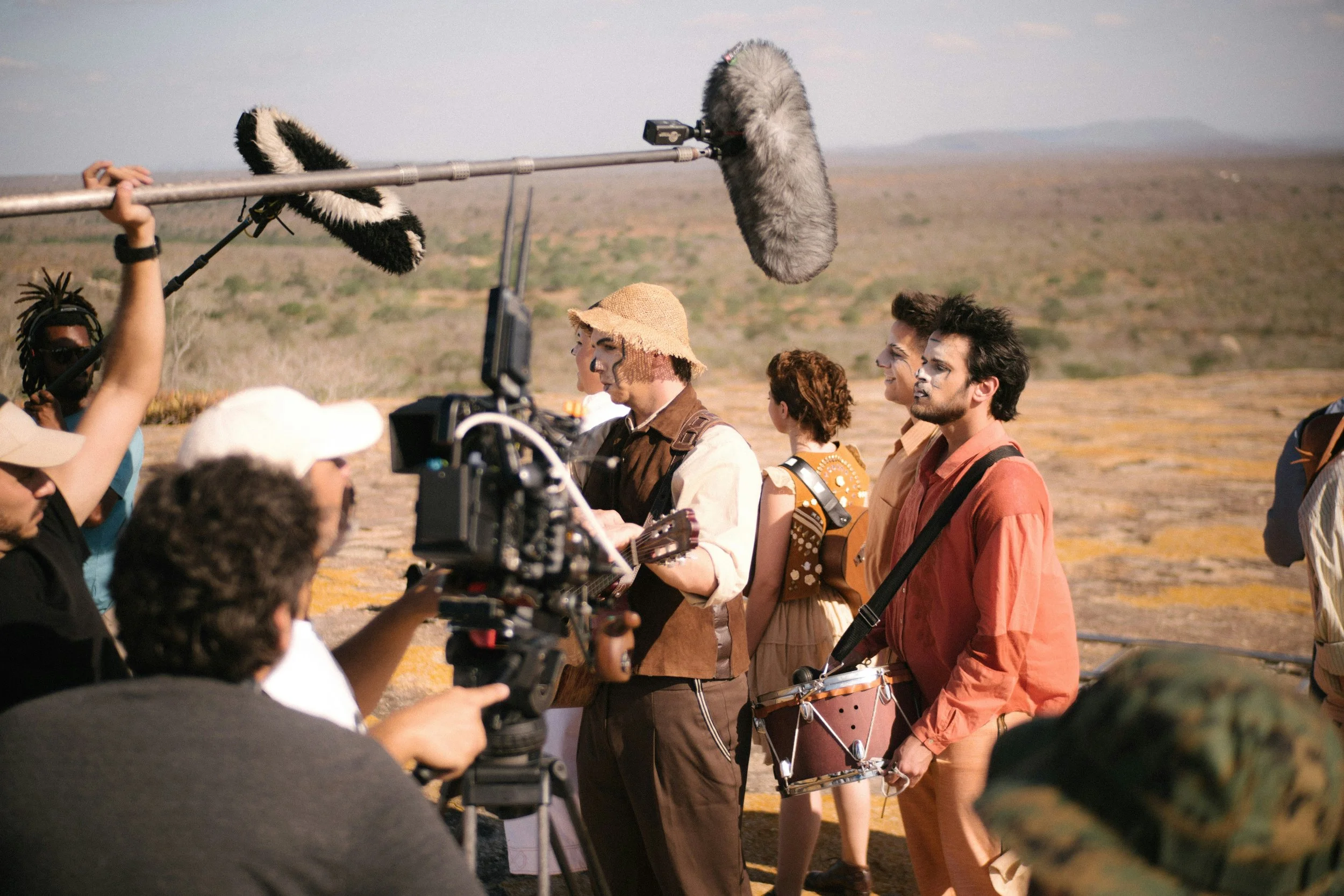 Film crew recording musicians in an outdoor desert setting, with boom microphones and camera equipment.
