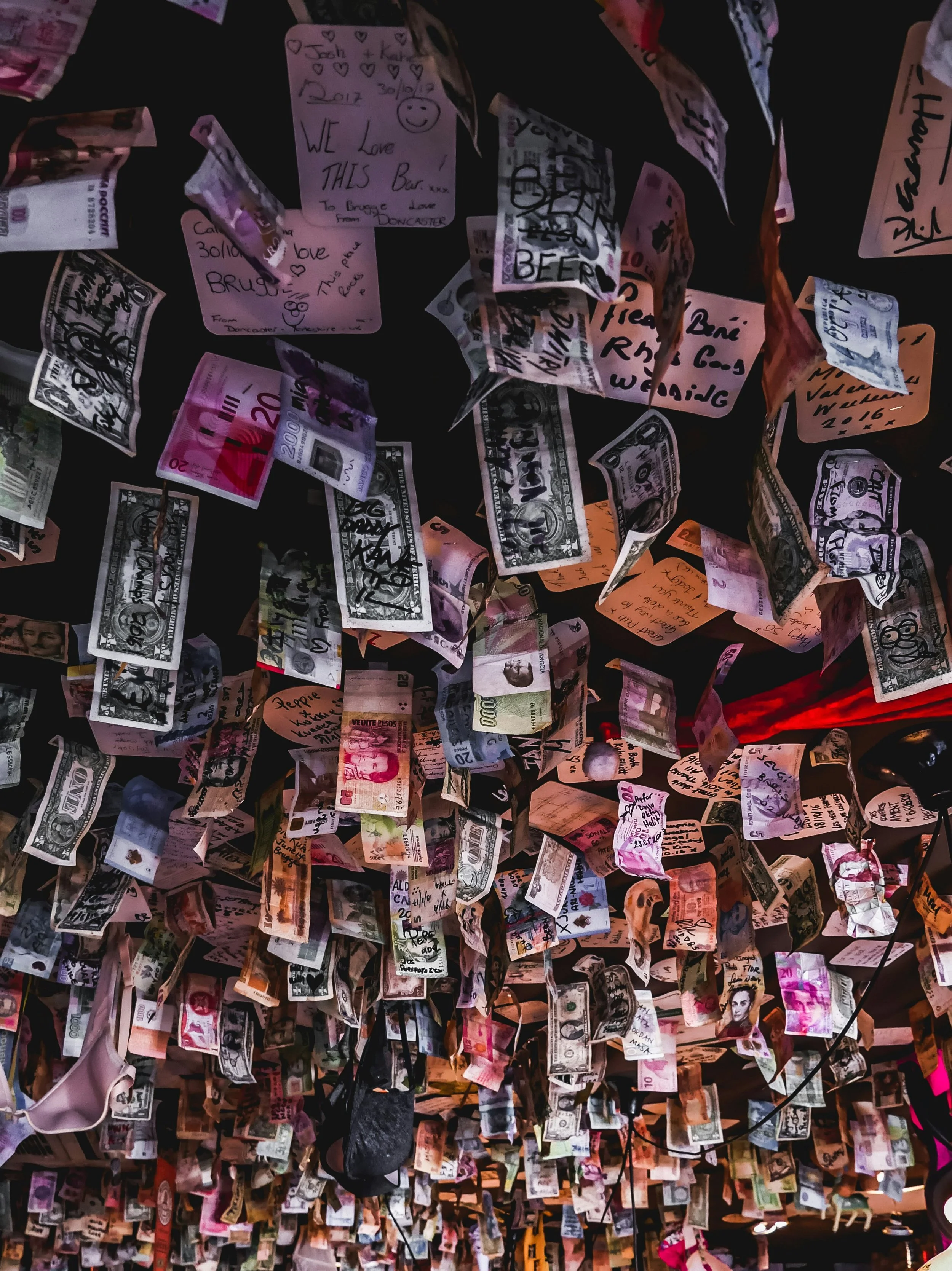 ceiling decorated with numerous hanging paper notes and various currency bills, including U.S. dollar bills and international banknotes, some with handwritten notes and messages.