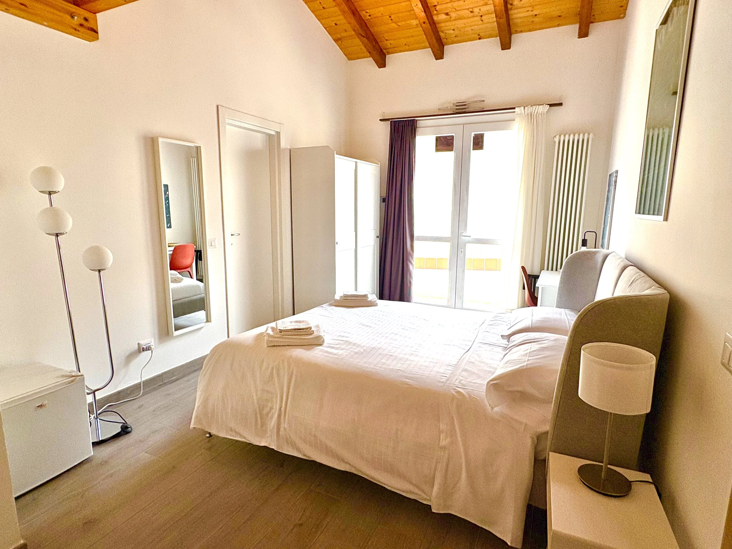 Sunlit guest room with wood-beam ceilings and neutral décor at The Club House Bordighera