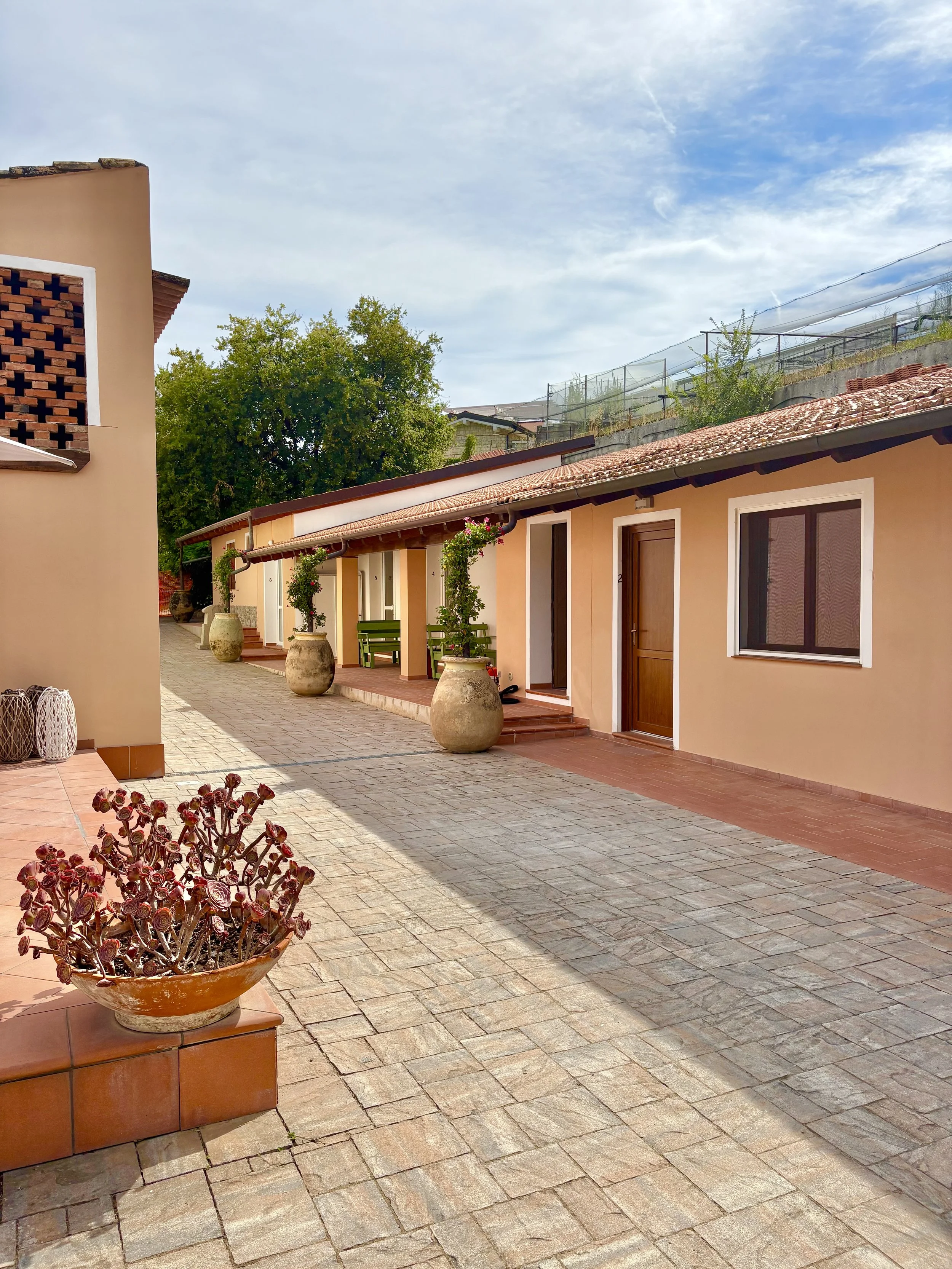 Exterior view of The Club House guest rooms in Bordighera with shared courtyard and rustic ceramic planters