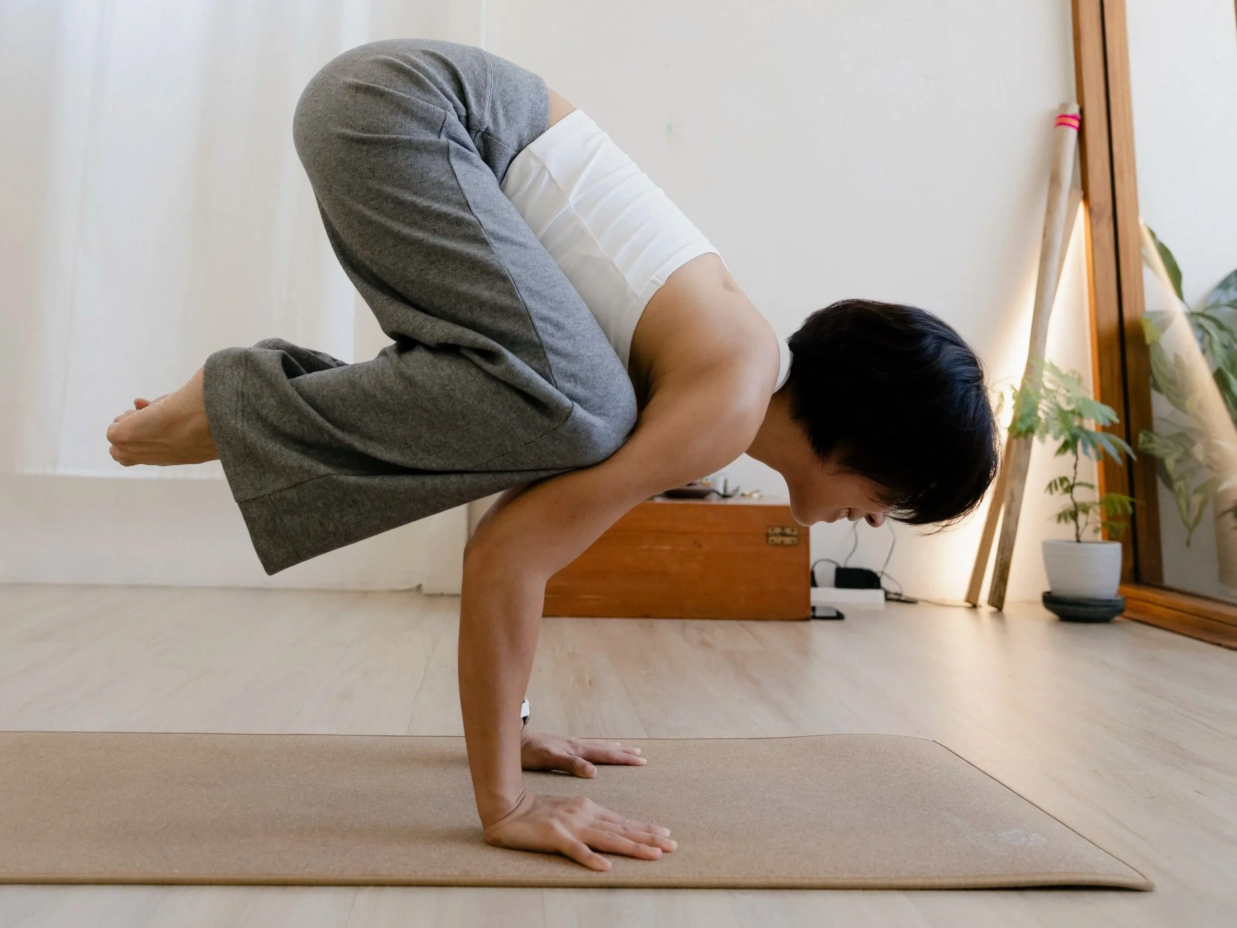 A woman with short black hair wearing a red spaghetti strap crop top smiling and sitting on a chair.