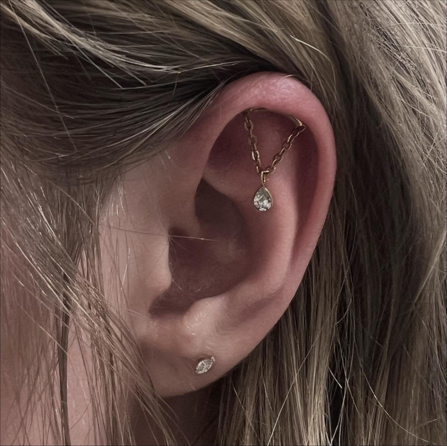 Close-up of a person's ear with a gold chain and diamond teardrop earring and a diamond stud piercing.