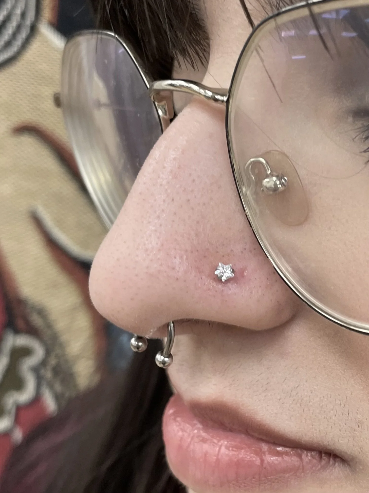 Close-up of a woman's face showing her nose with a septum piercing, eye makeup, and orange-red lipstick.