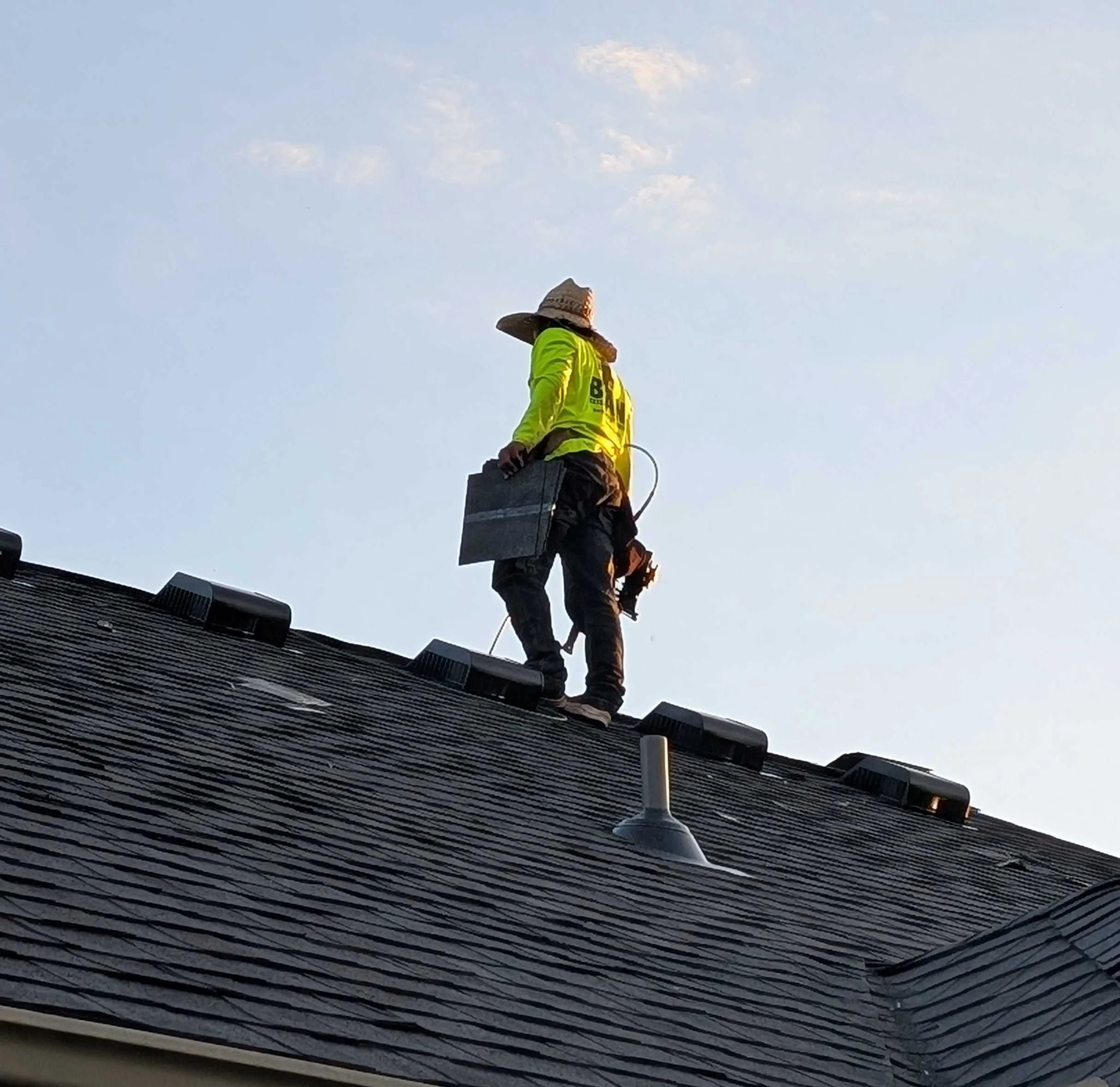 Bean crew member on a residential roof with shingles in hand