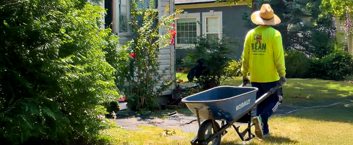 Bean team member hauling old shingles in a wheel barrow