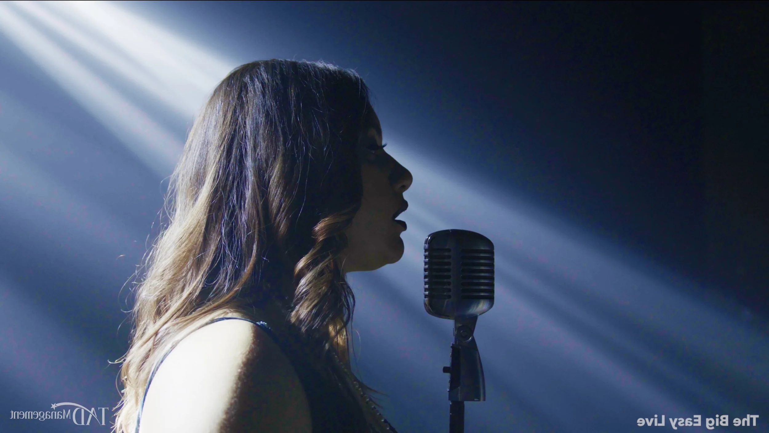 A woman singing into a vintage microphone on stage, with concert lighting creating a dramatic silhouette.