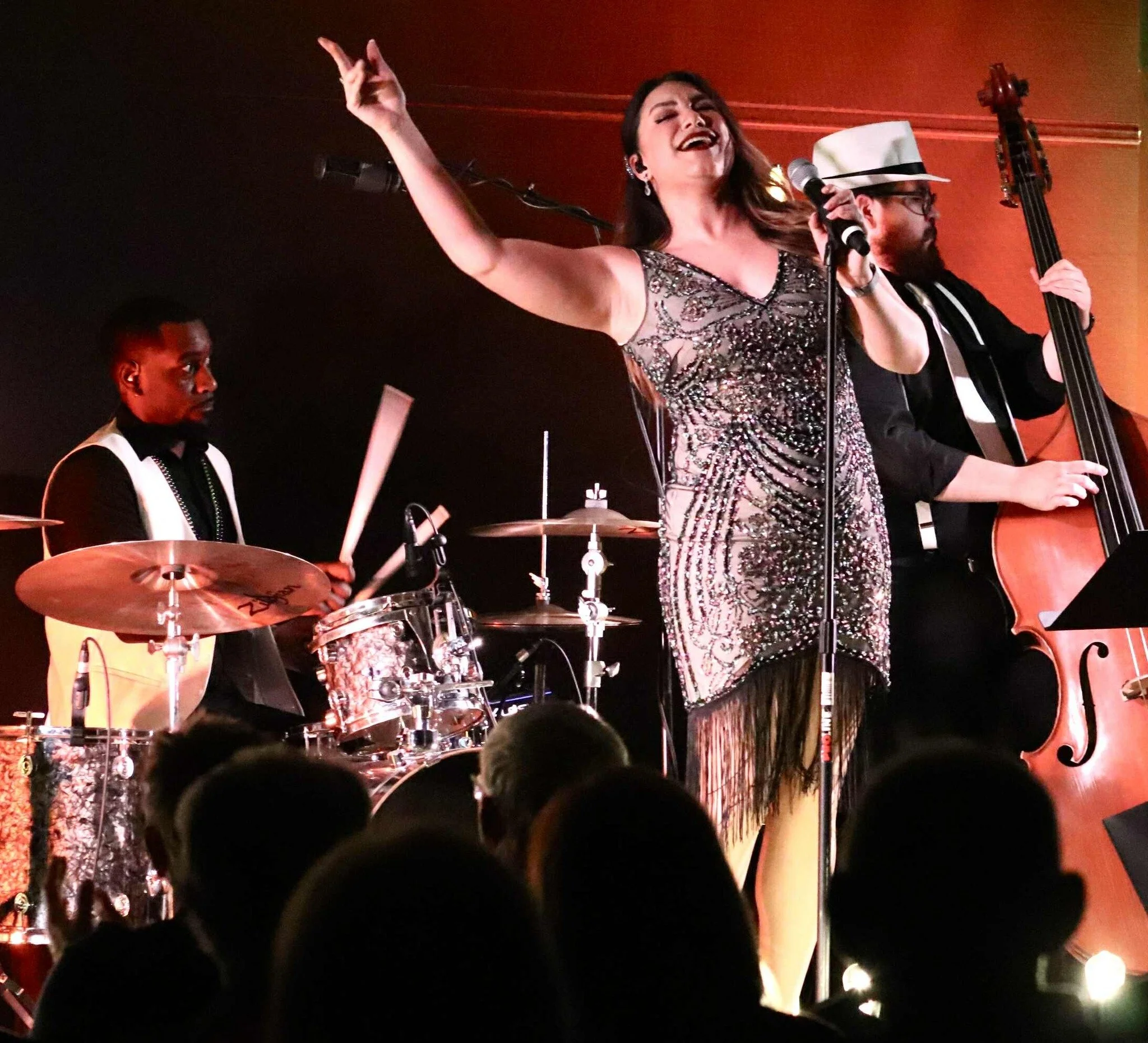 A woman singing passionately into a microphone with a band playing instruments behind her at a live music performance.