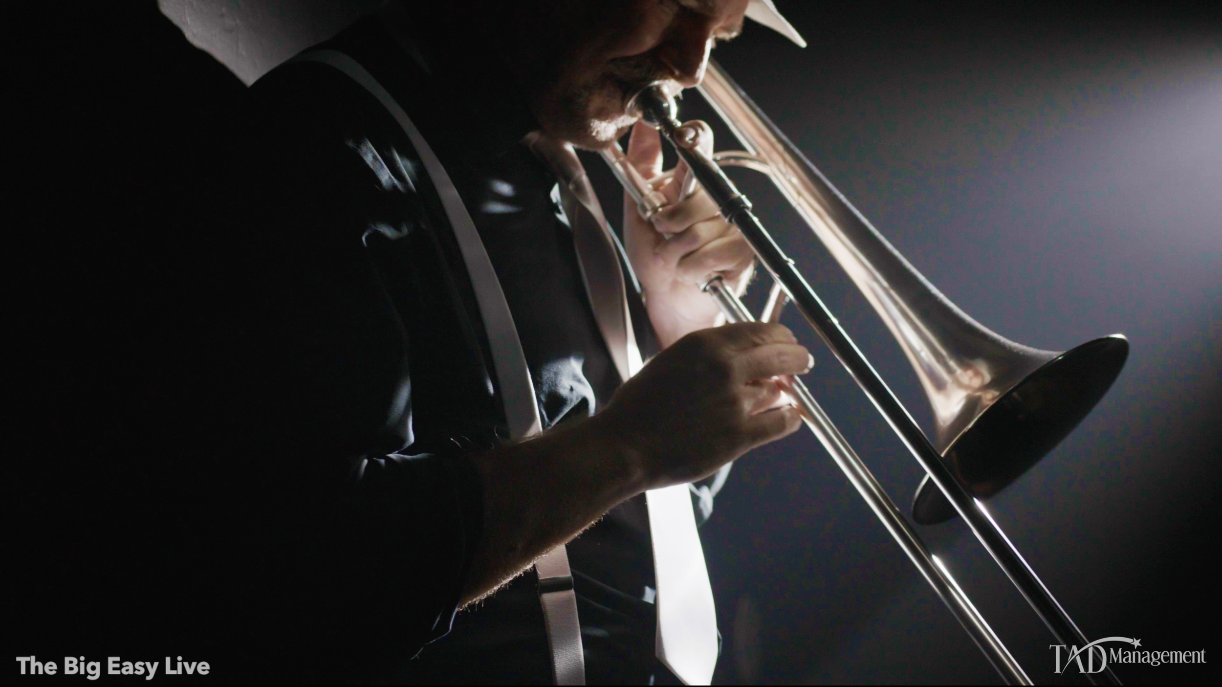 A man playing a trombone in a dark setting, with a light source illuminating the instrument and part of his face.