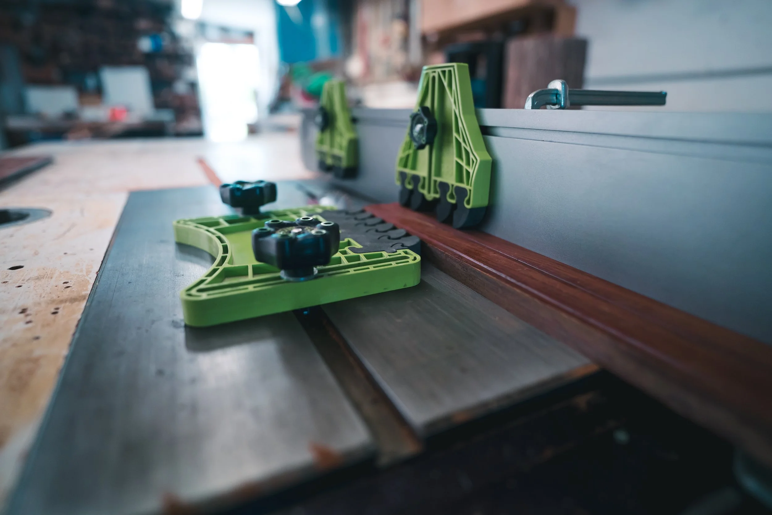 Close-up of a woodworking table saw with green and black safety features, in a woodworking workshop.