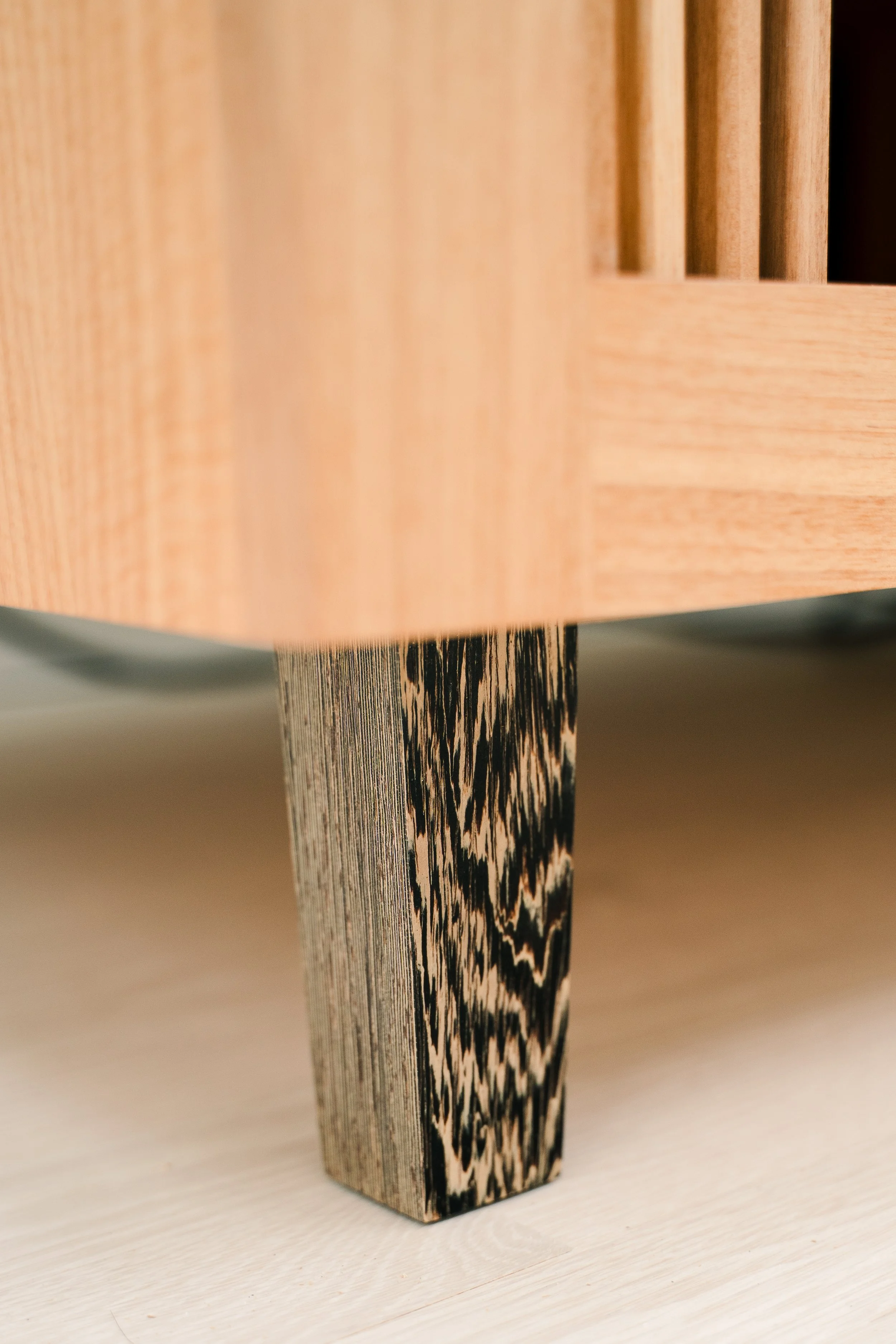 Close-up of a wooden furniture leg with a black and tan wood grain pattern, supporting a light-colored wooden piece.