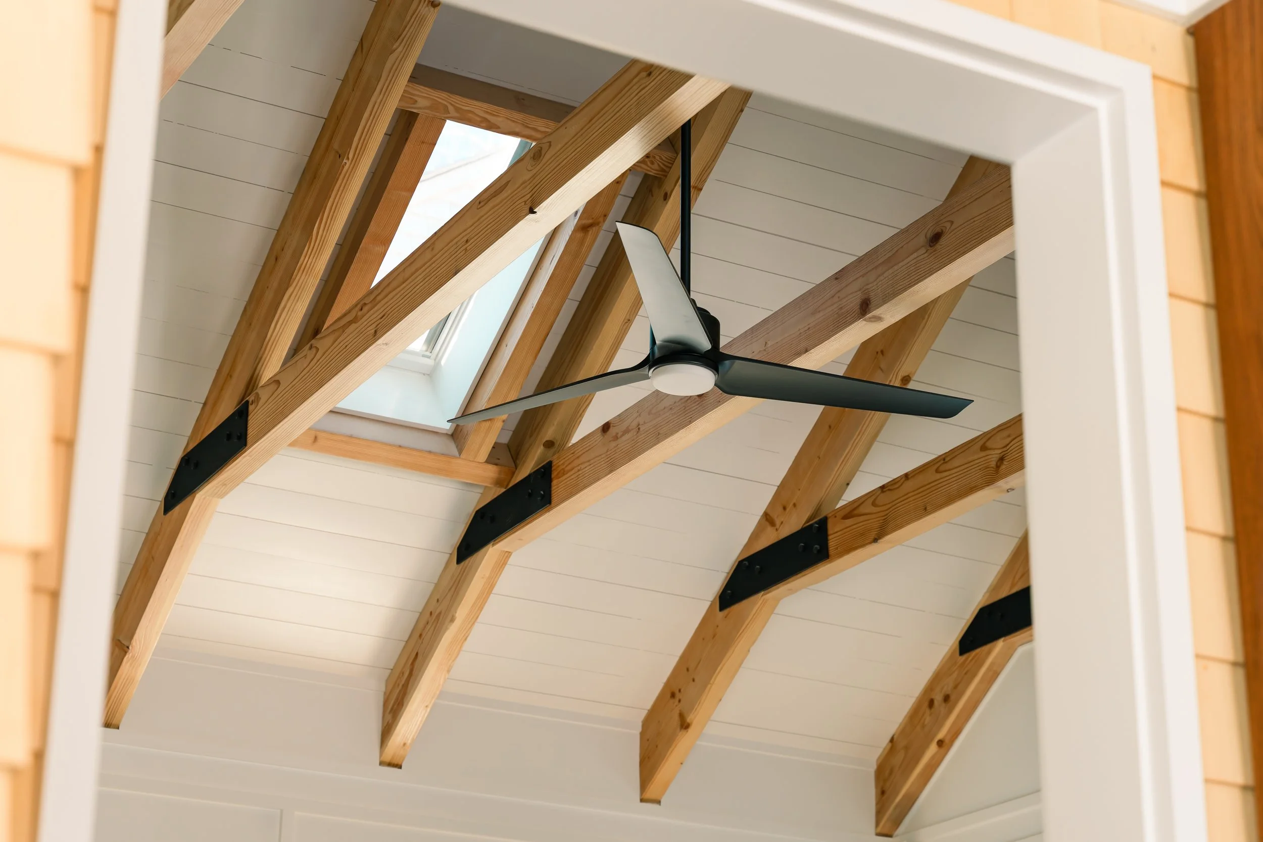 A ceiling with exposed wooden beams, a skylight window, and a modern black ceiling fan.