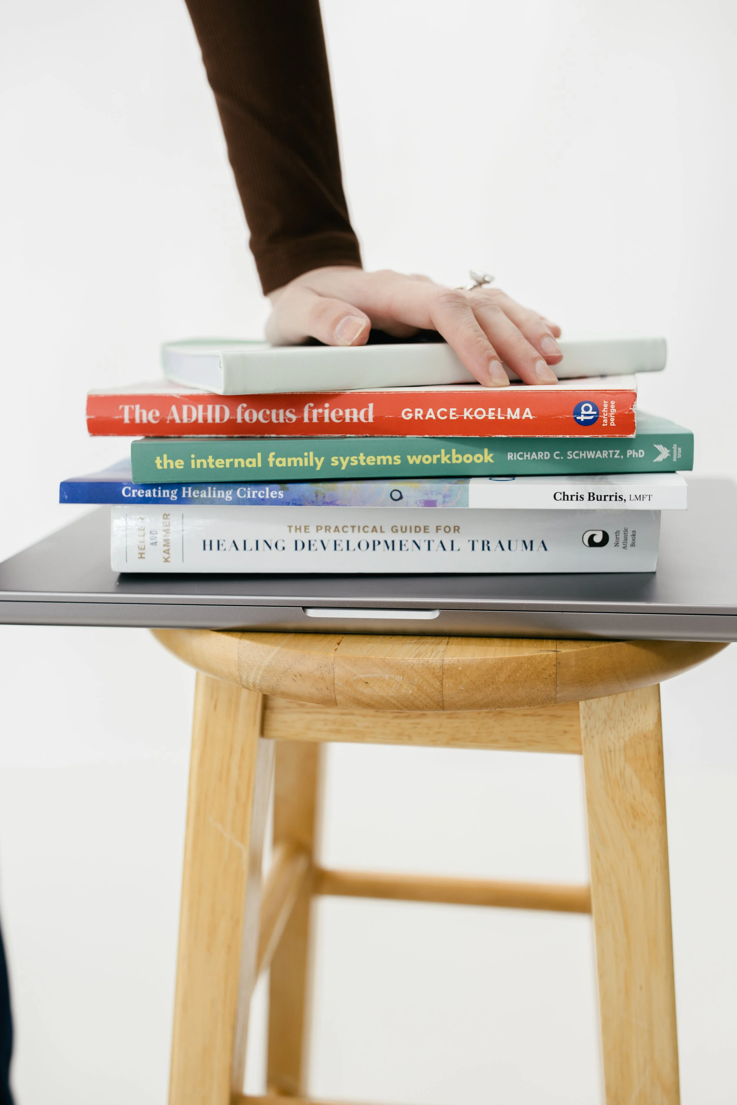 Stack of clinical books on ADHD and Internal Family Systems therapy on a wooden stool