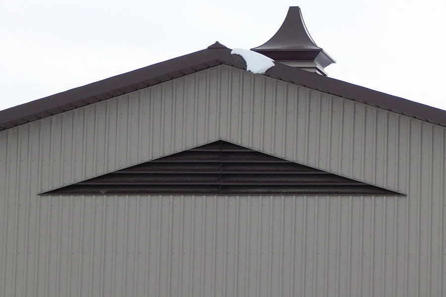 Close-up view of the roof of a building with snow on it, featuring a peaked structure and a vent or chimney.
