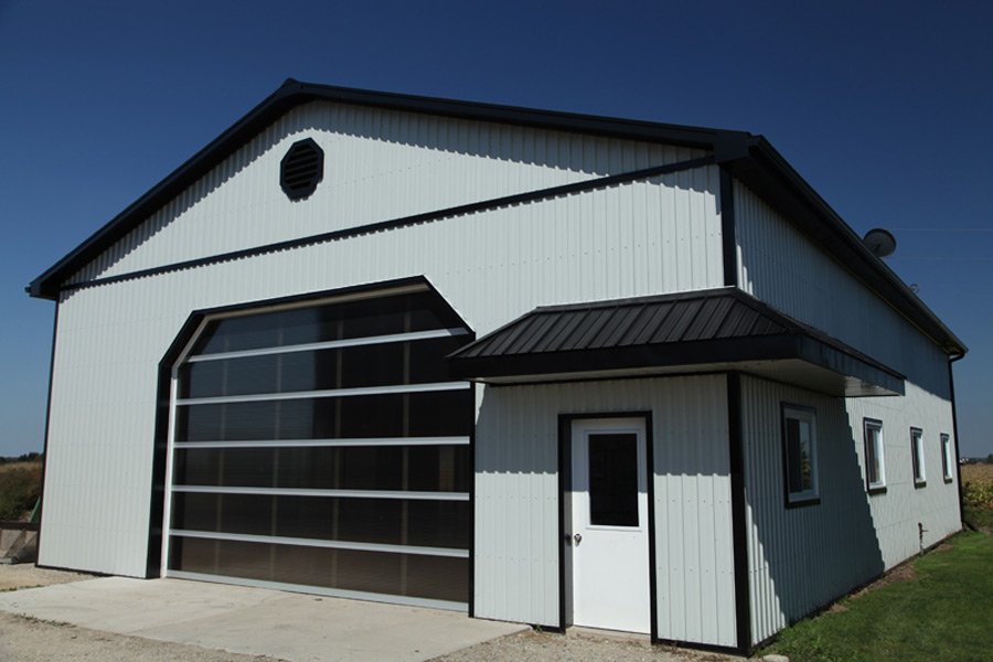 A large white metal building with a garage door and a side entrance, situated in an open area with a clear blue sky.