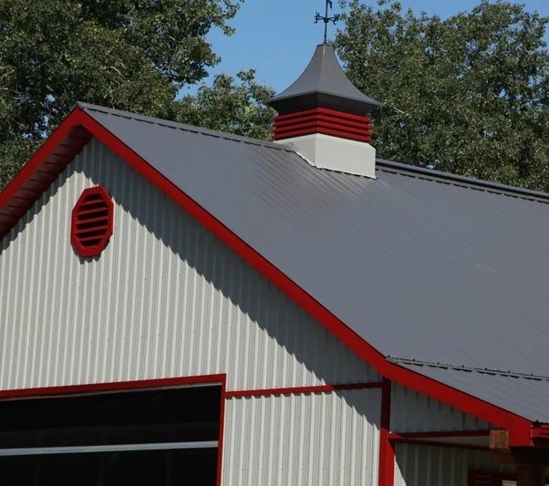 Close-up of a building's roof with a weather vane, painted white and red, under a blue sky with trees in the background.