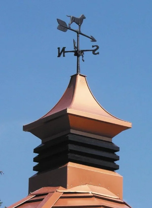 Close-up of a rooftop with a weather vane featuring a dog on top, against a blue sky.