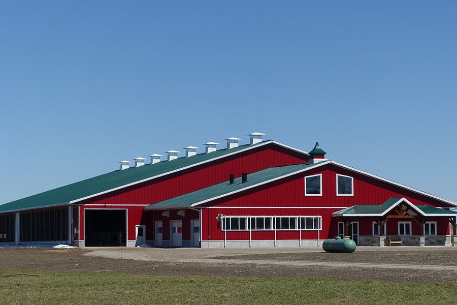 Large red barn with green roof, surrounded by open field and clear blue sky.