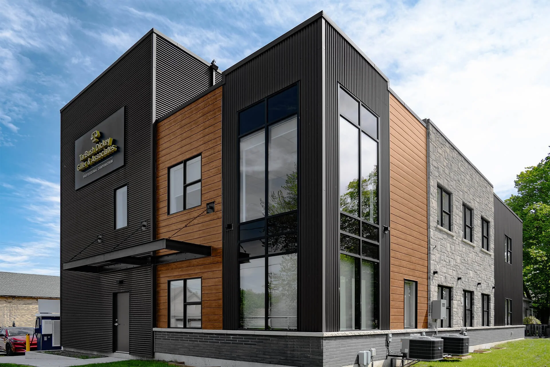 Modern multi-story office building with black metal, wood, and stone exterior, large windows, and a sign that reads "Tar Bush, Giller & Associates".