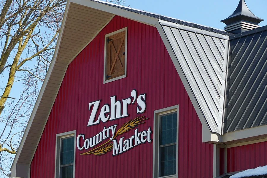 Red barn-style building with a sign that reads 'Zehr's Country Market' and has a small window and wooden barn door near the roof.