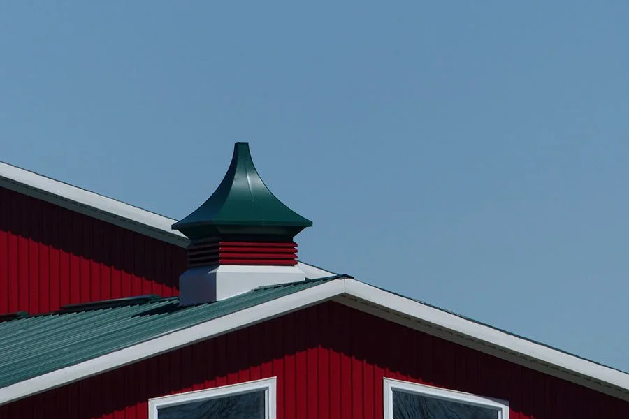 Close-up of a red building with a green metal roof and a decorative green and red cupola on top, under a clear blue sky.