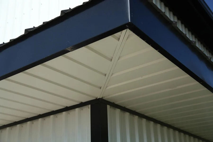 Close-up of the corner of a building's roof with black trim and white metal siding panels.